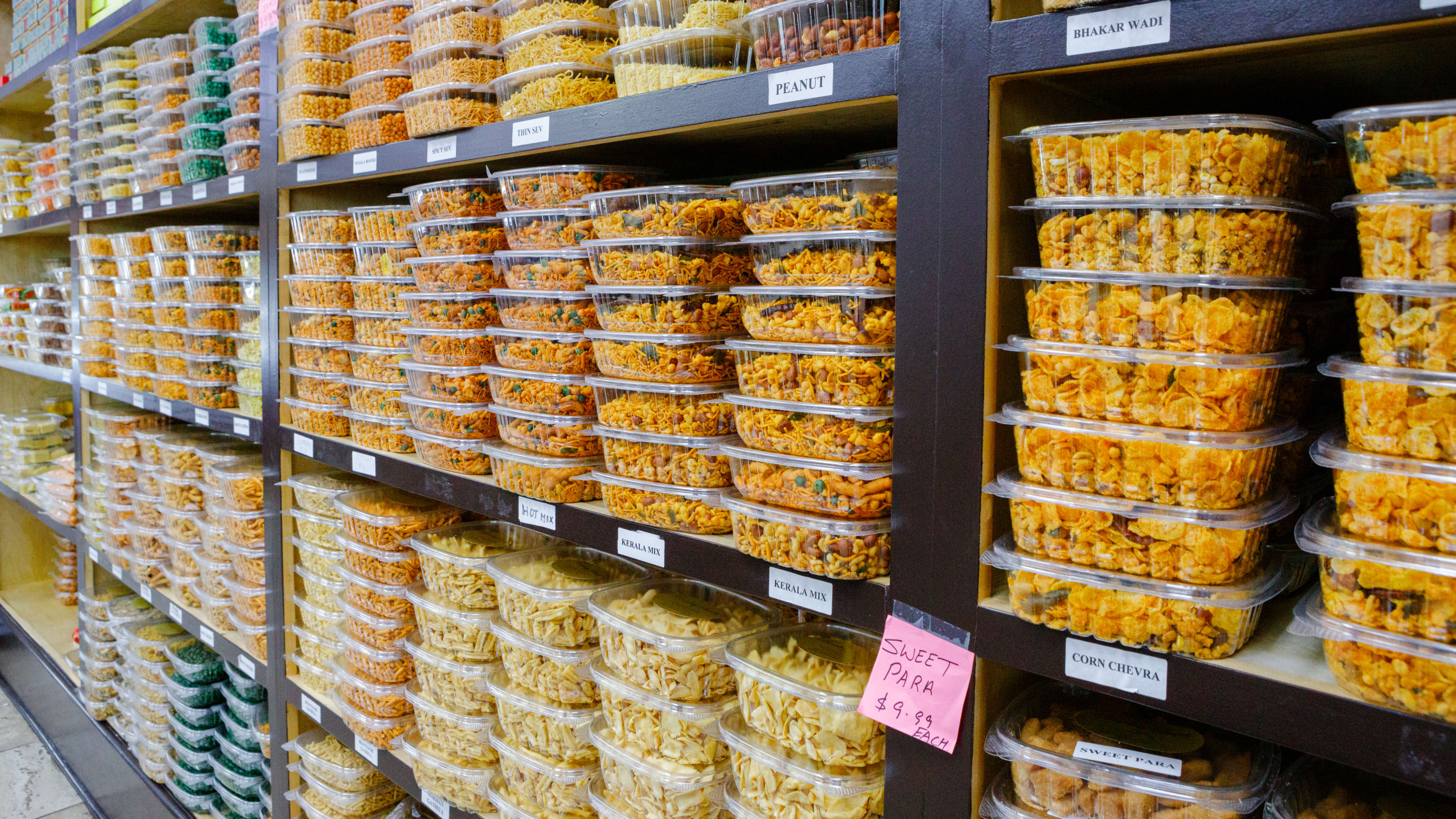 snack mixes in plastic containers on shelves at Bombay Sweets.