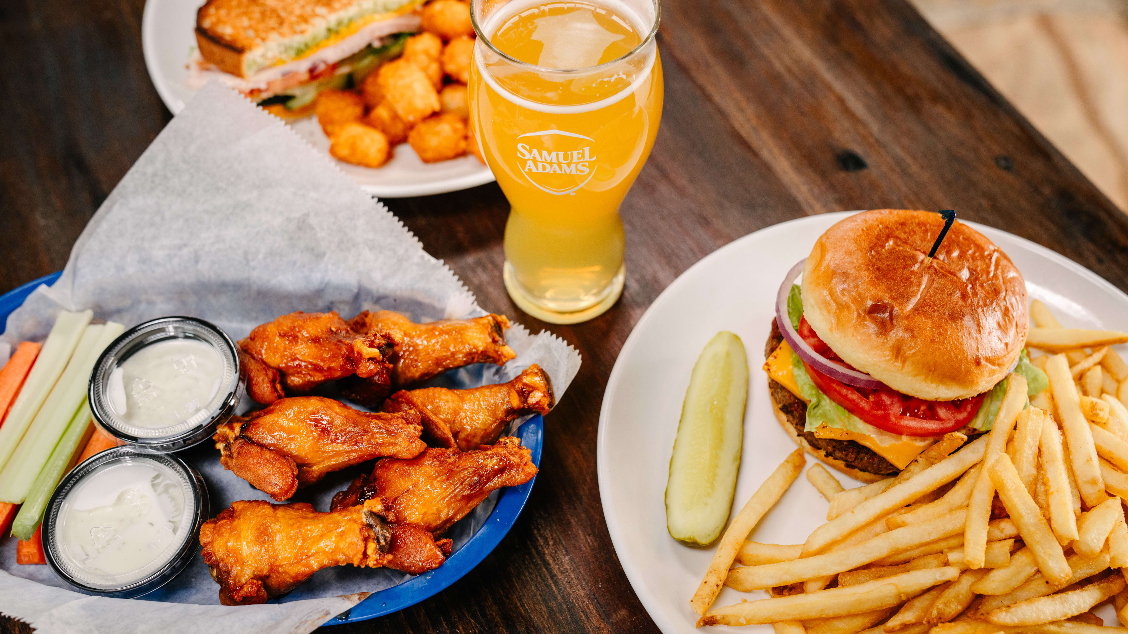 A table spread with wings, a cheeseburger, fries, and tater tots.