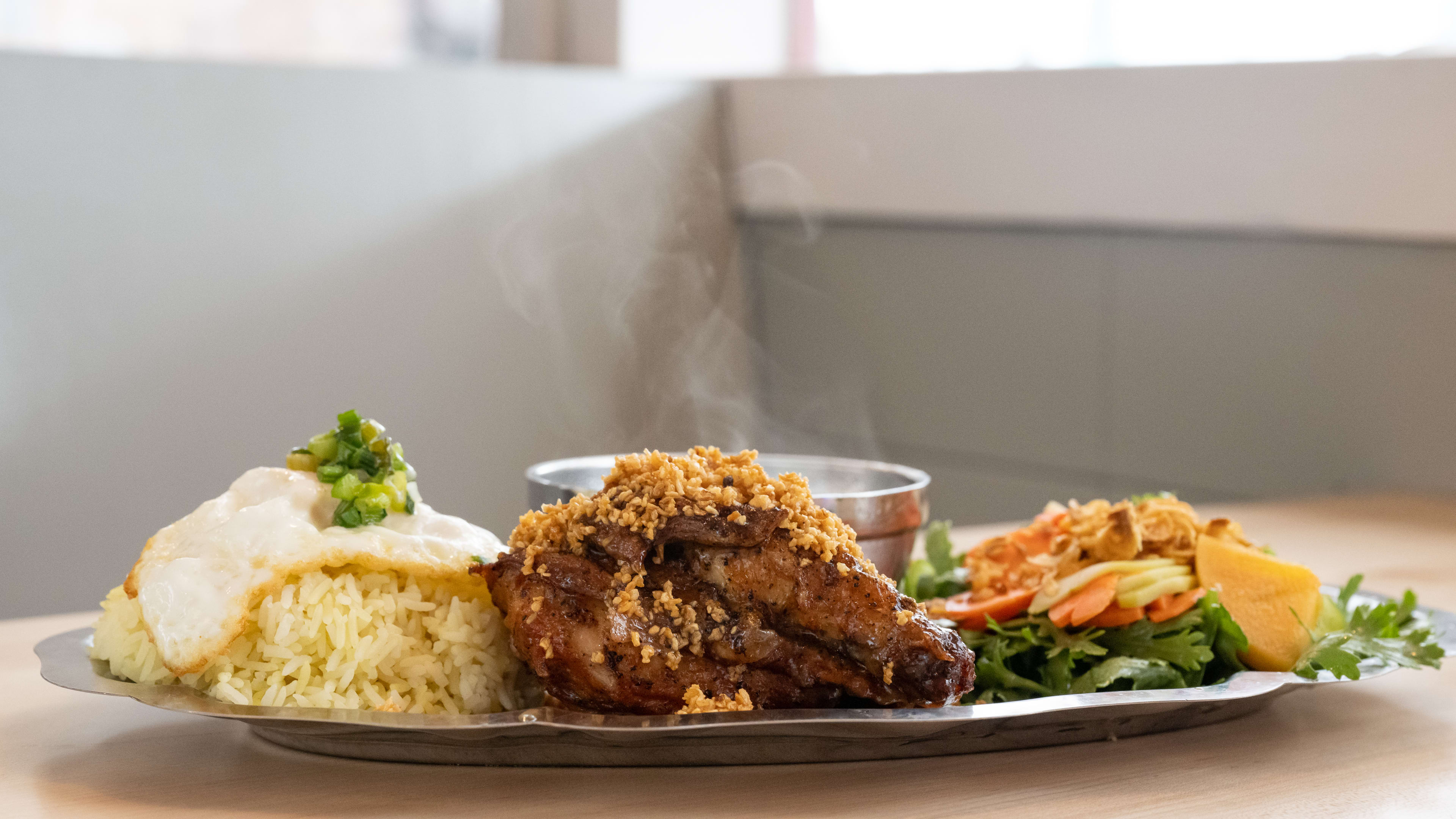 Plate of rice with a fried egg on top, some chicken wings, and greens on the side.