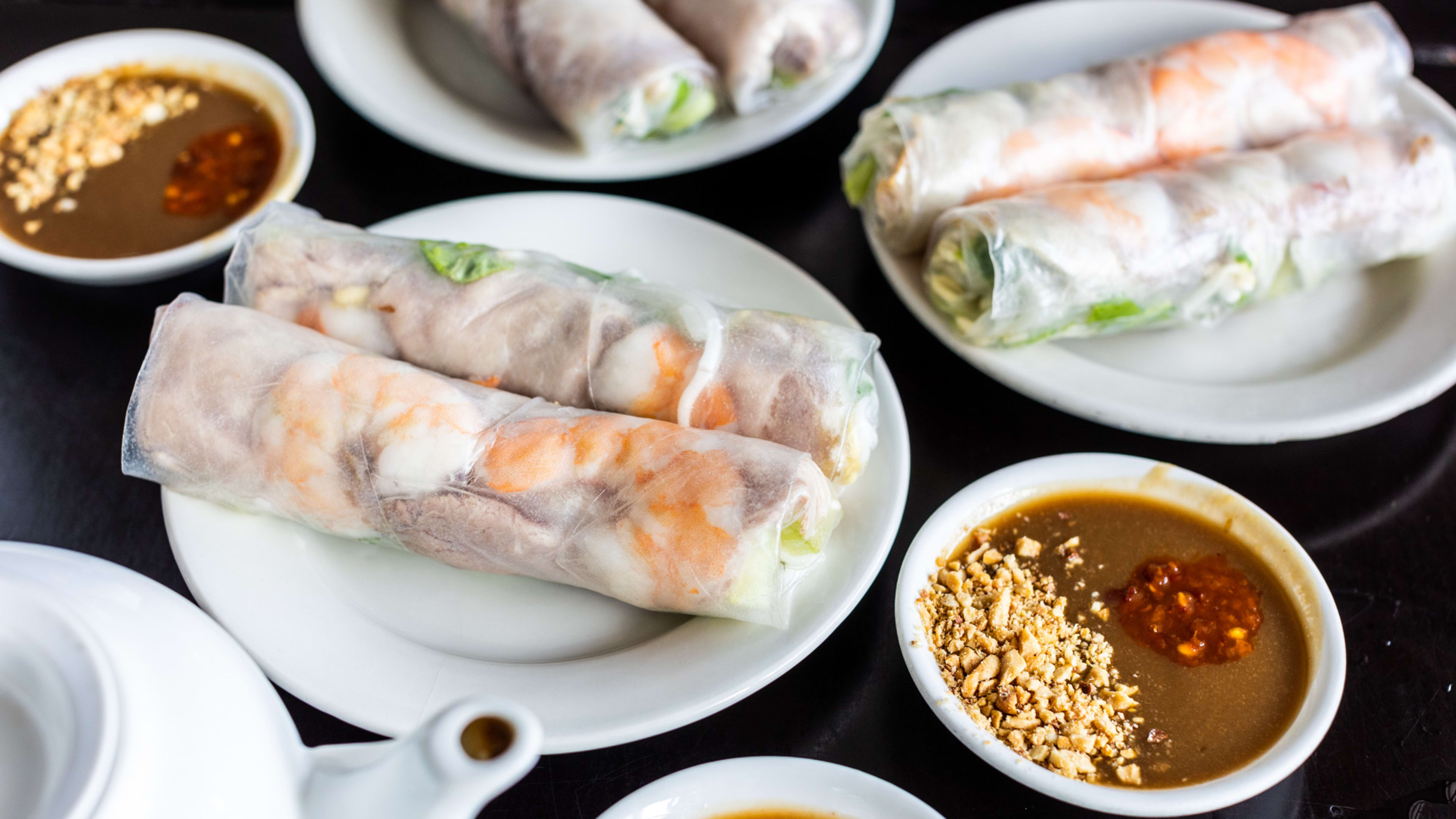 Three different kinds of spring rolls, two on each plate. The shrimp and pork spring roll is in the foreground with sauces on the side.