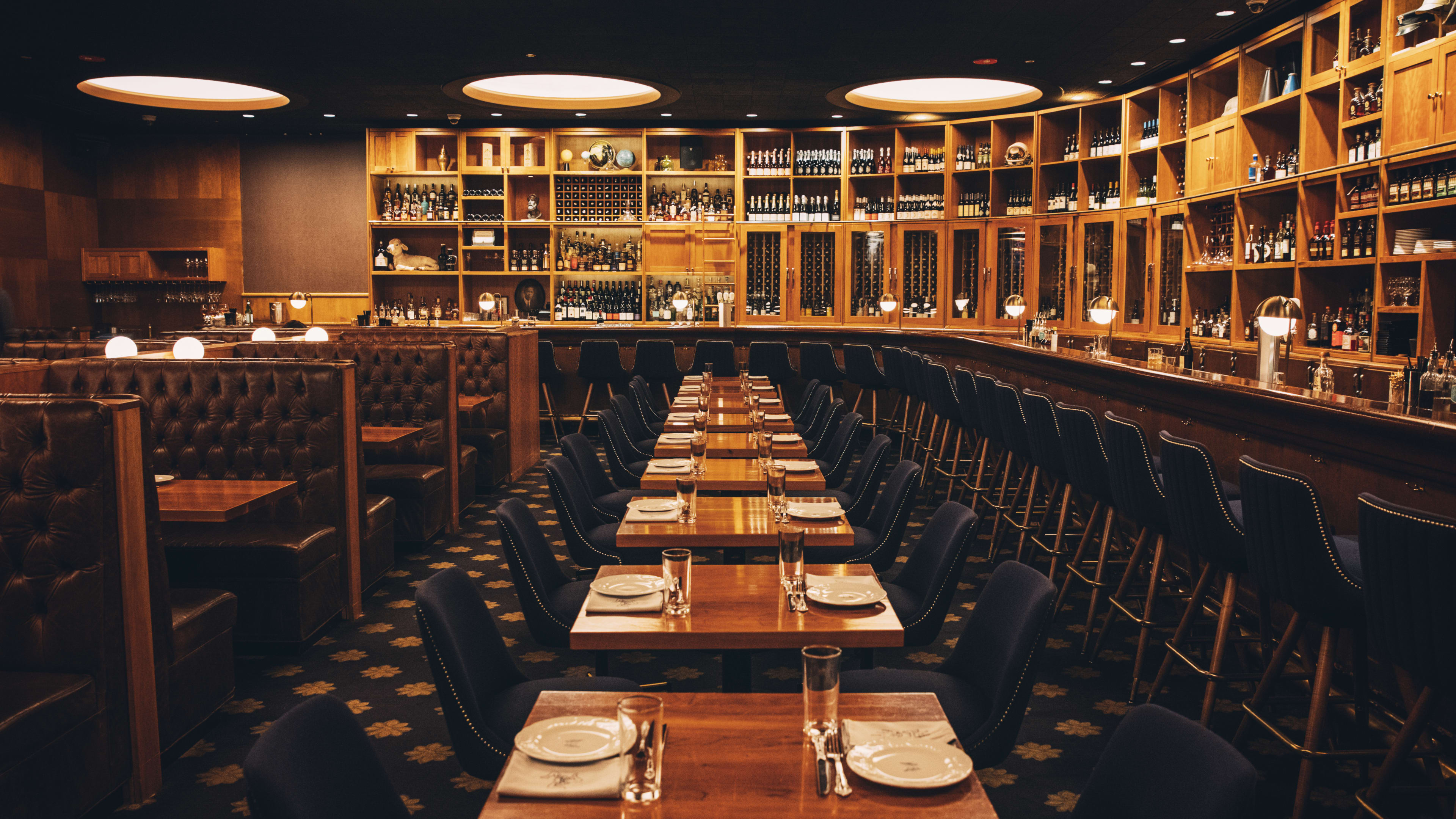 Long, wraparound wooden bar lined with wood shelves, and big leather booths