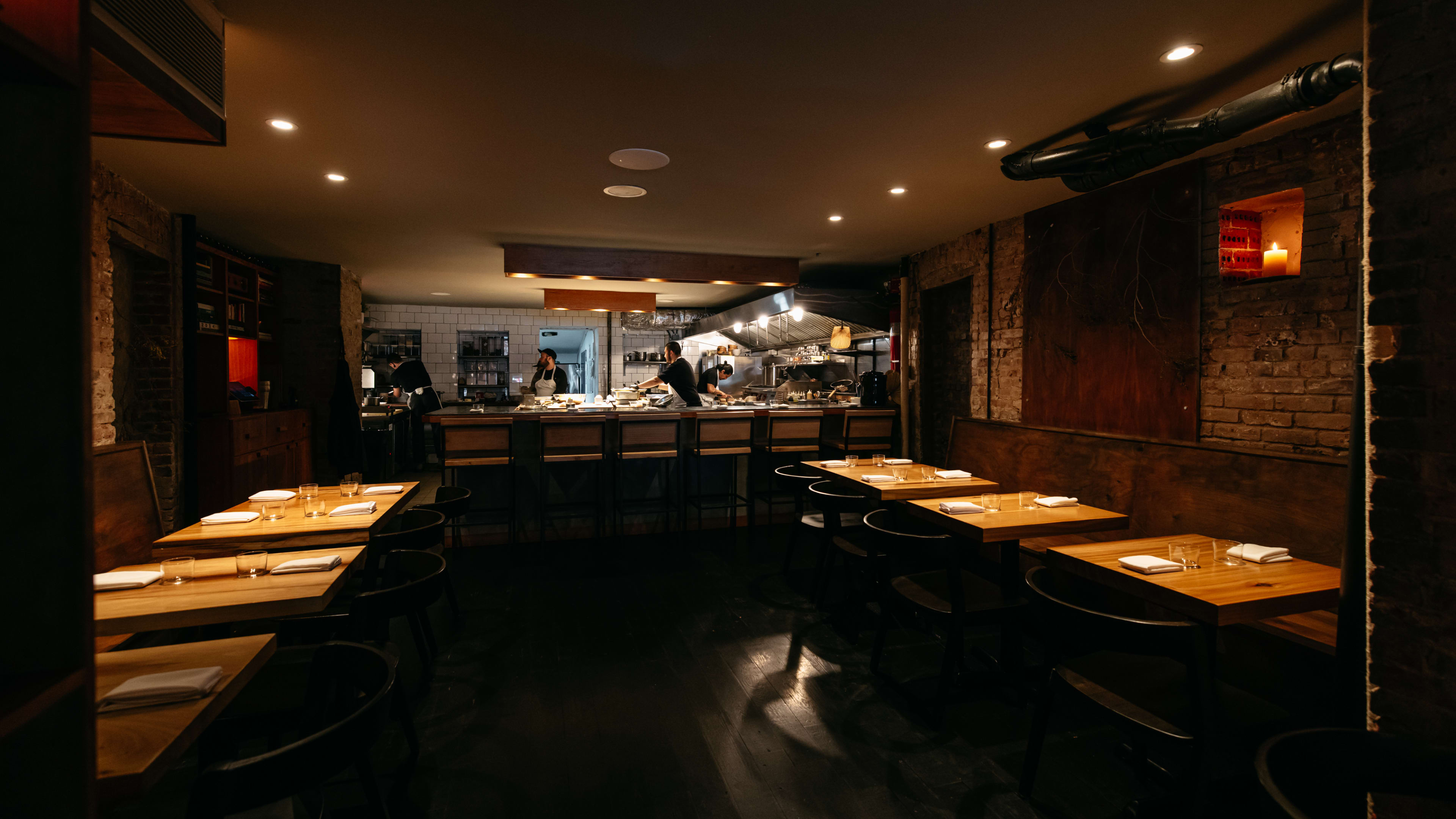 A dark dining room with brick walls and an open kitchen at the back.