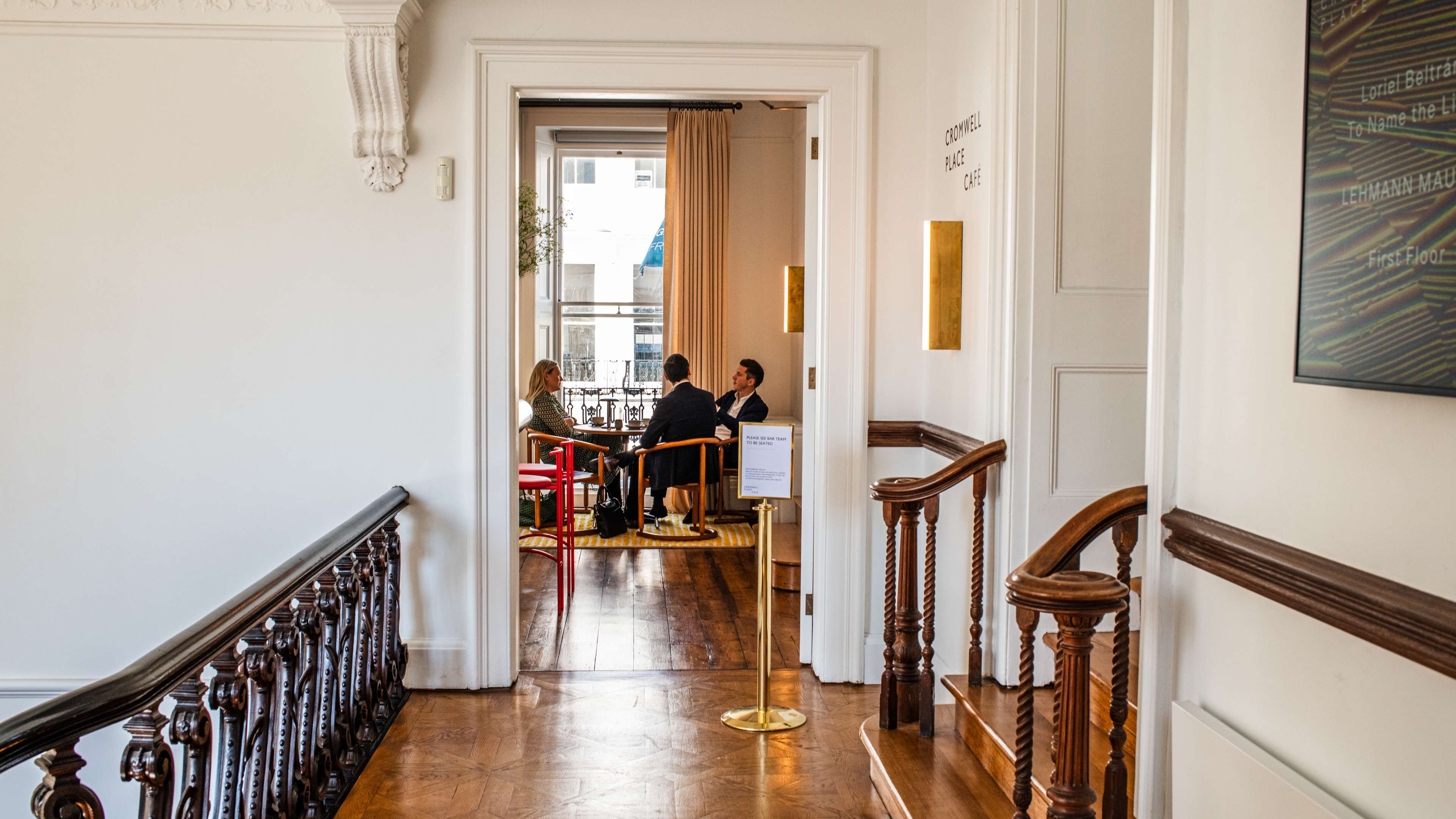 A hallway with wooden floors, leading to a cafe in the background.