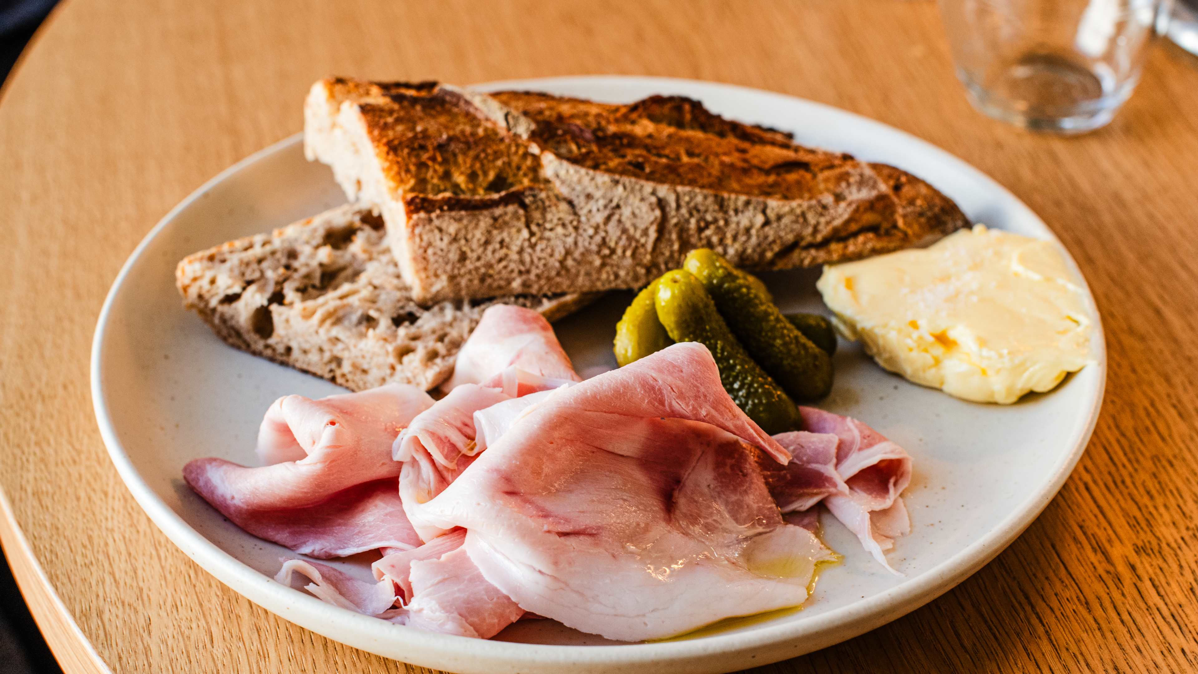 A plate of baguette, ham, pickles, and butter.