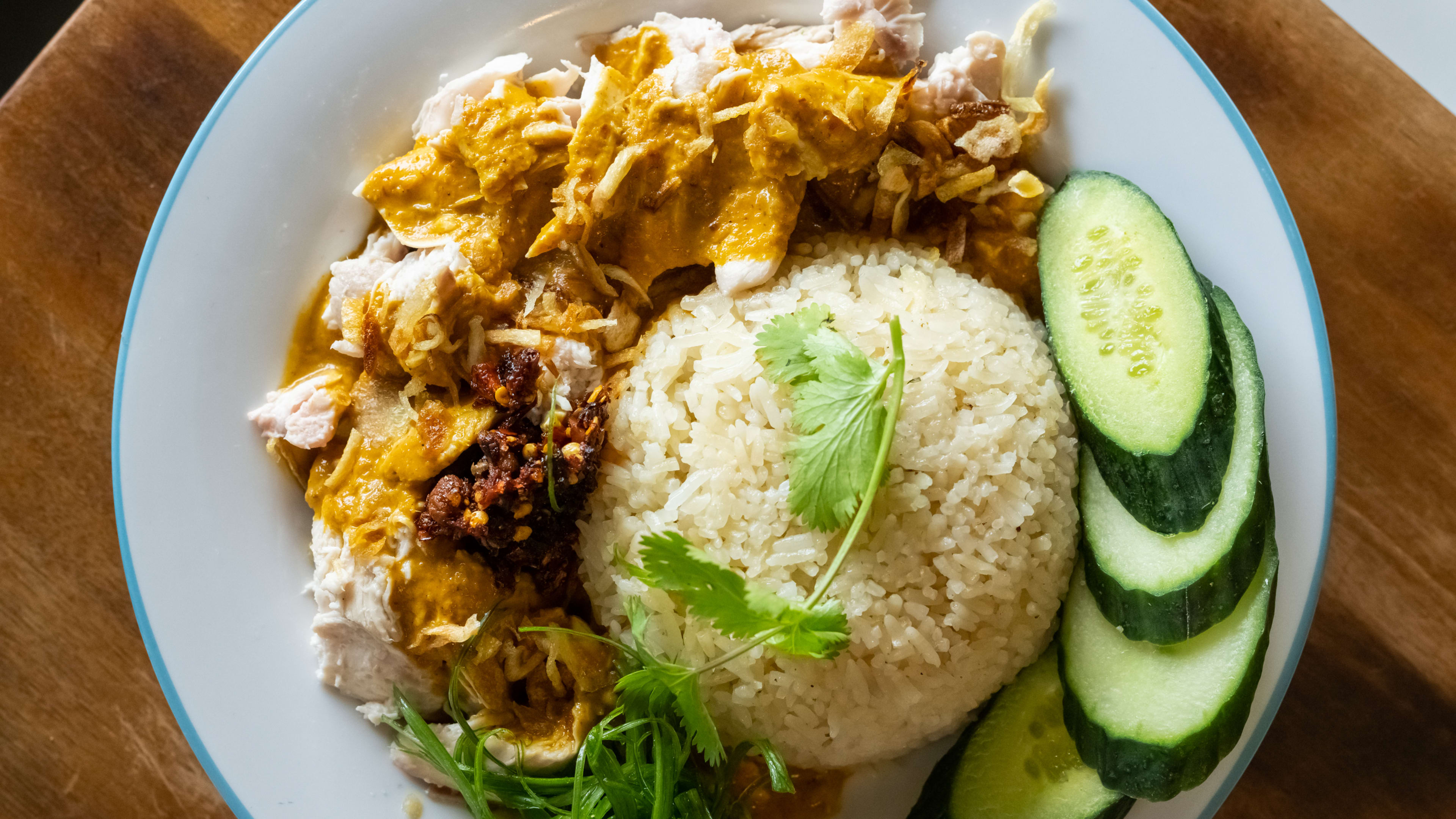 Plate of curry chicken with rice and raw cucumbers