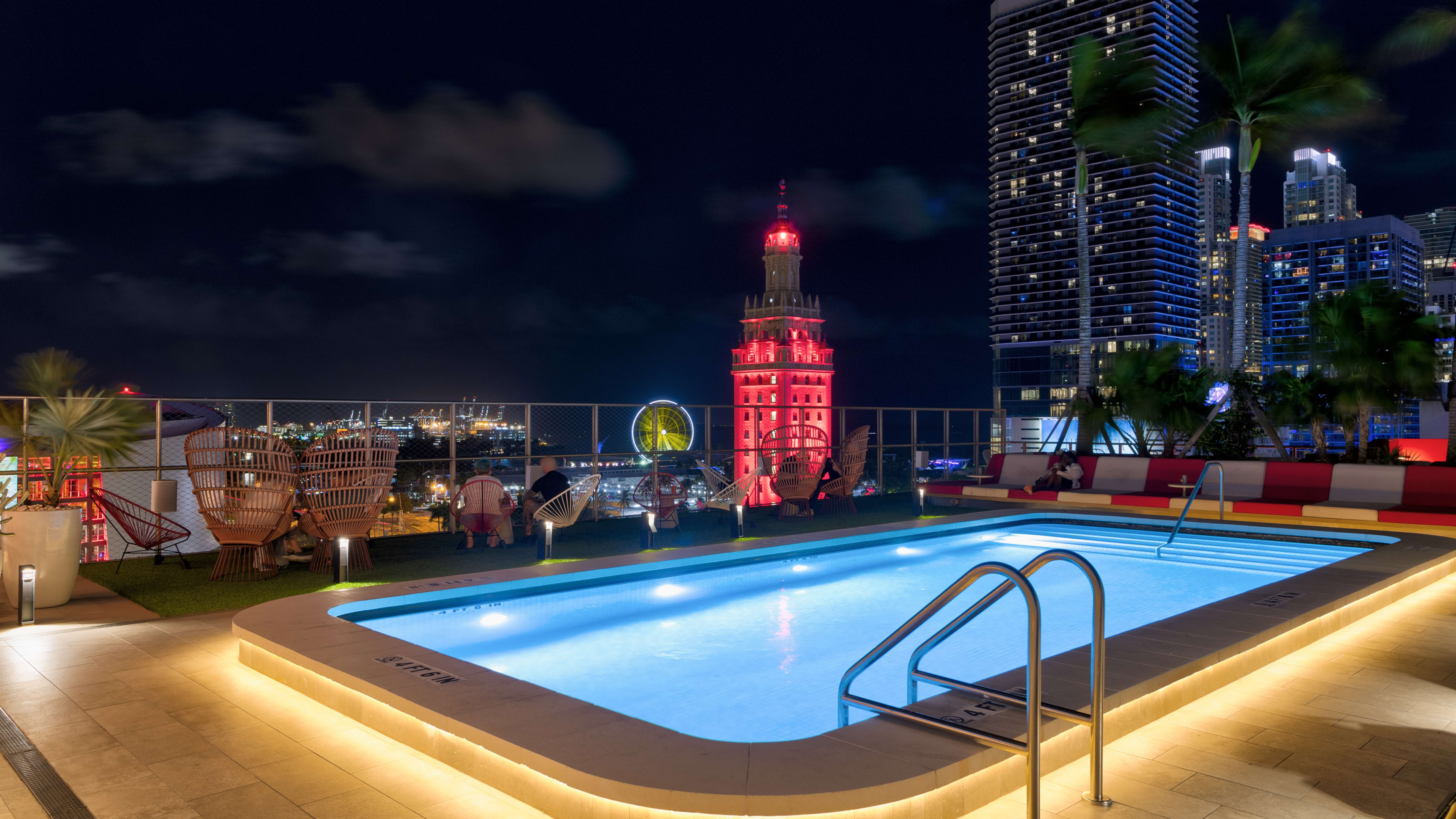 Rooftop pool with pool chairs surrounding it at night time.