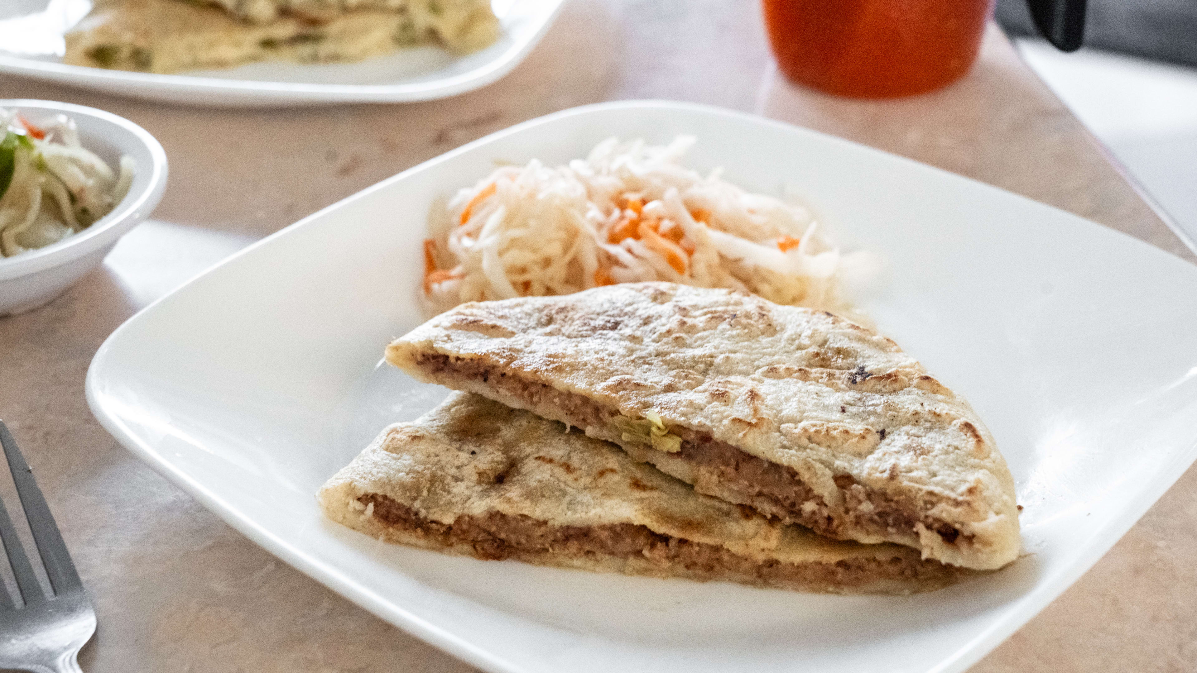 A pupusa cut in half on a plate.