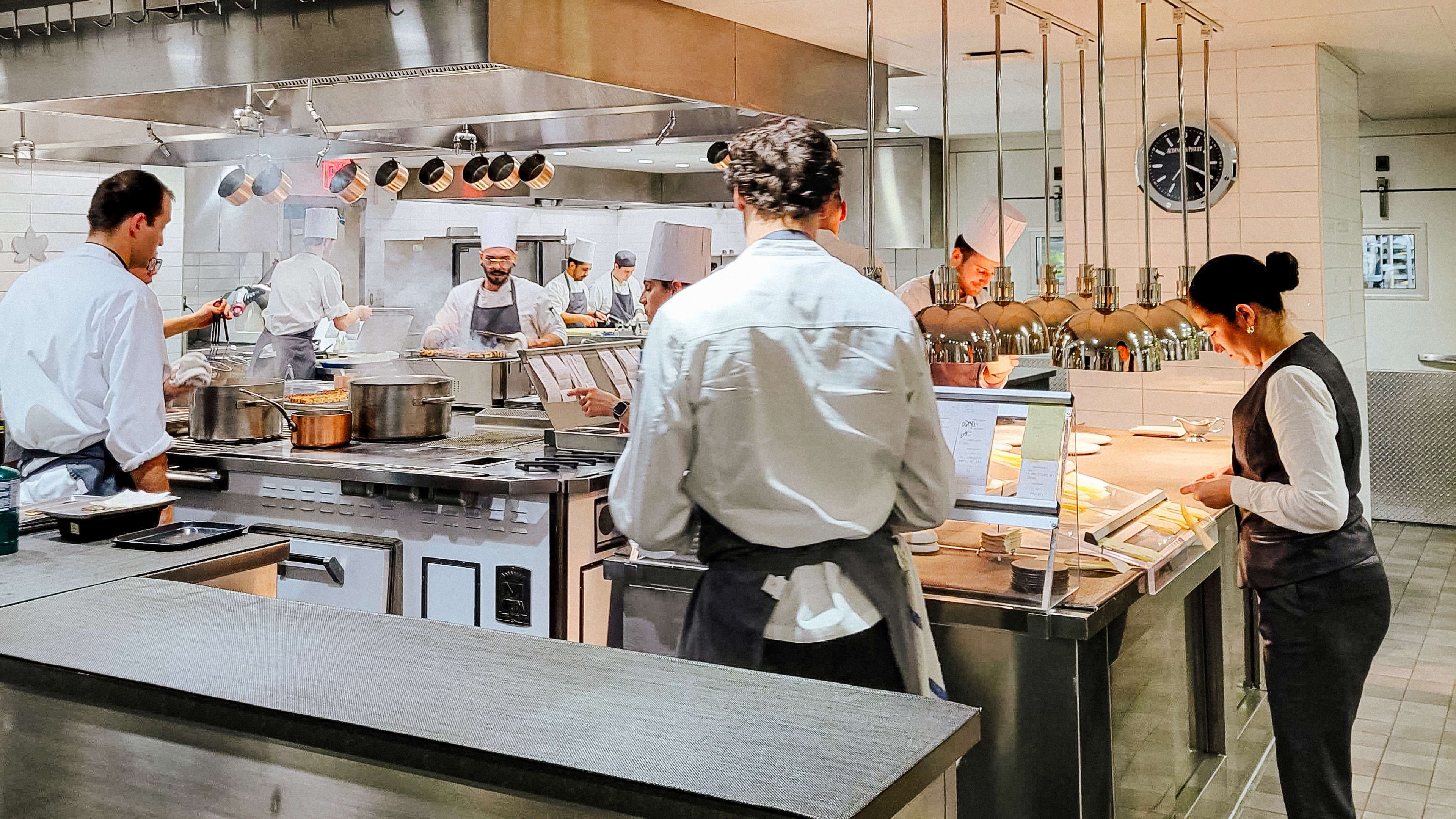 A big, bright restaurant kitchen filled with cooks in tall white hats.