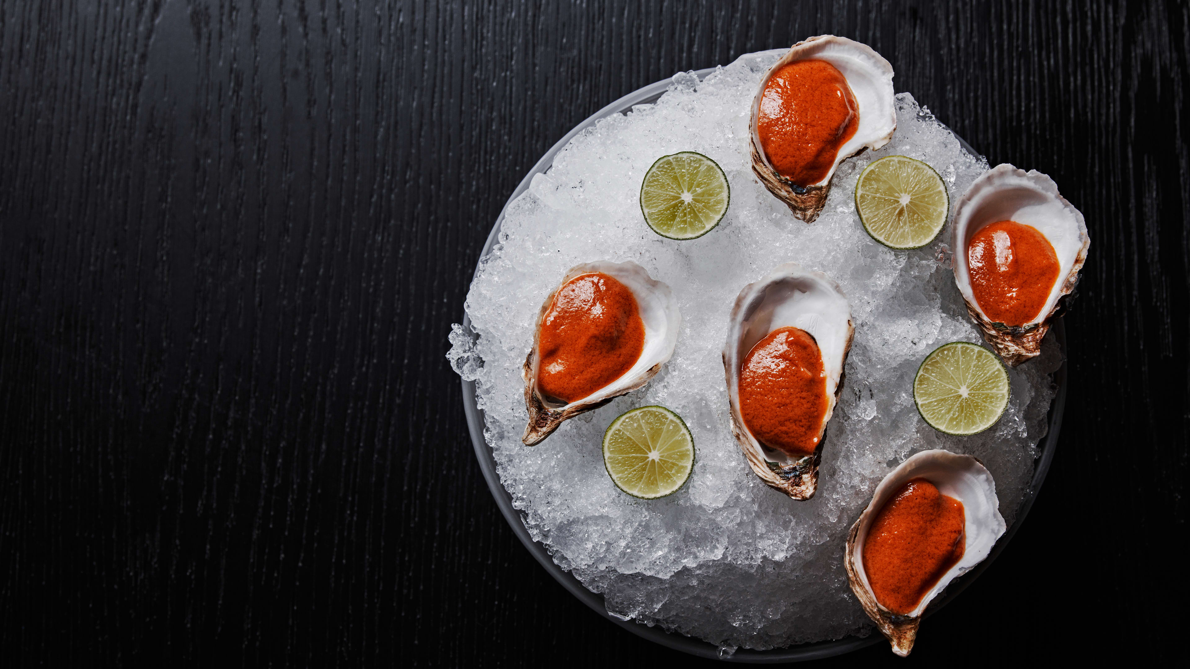 Five raw oysters arranged over ice with a thick red sauce over each.