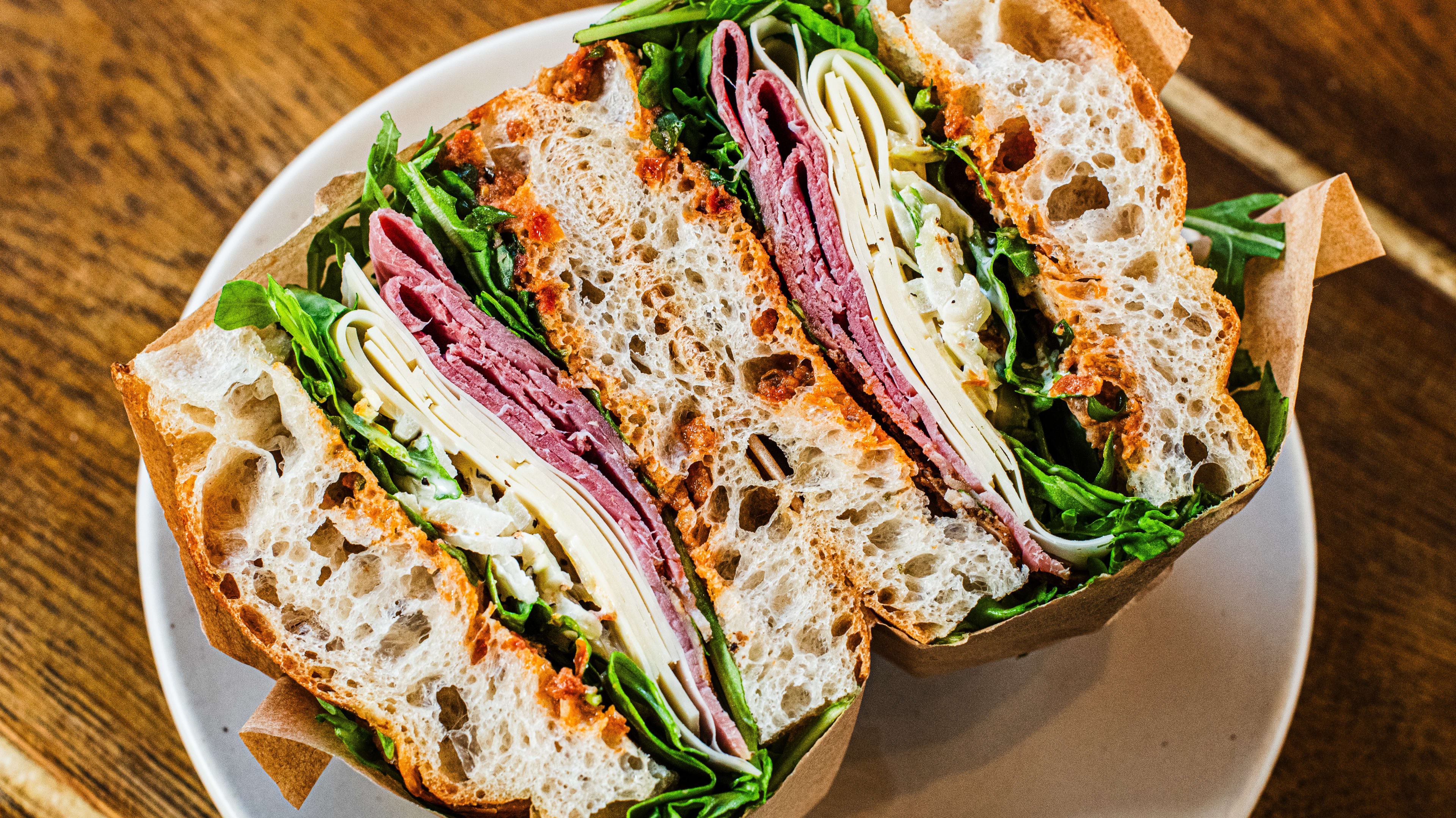 A pastrami sandwich on focaccia, cut in half on a plate.