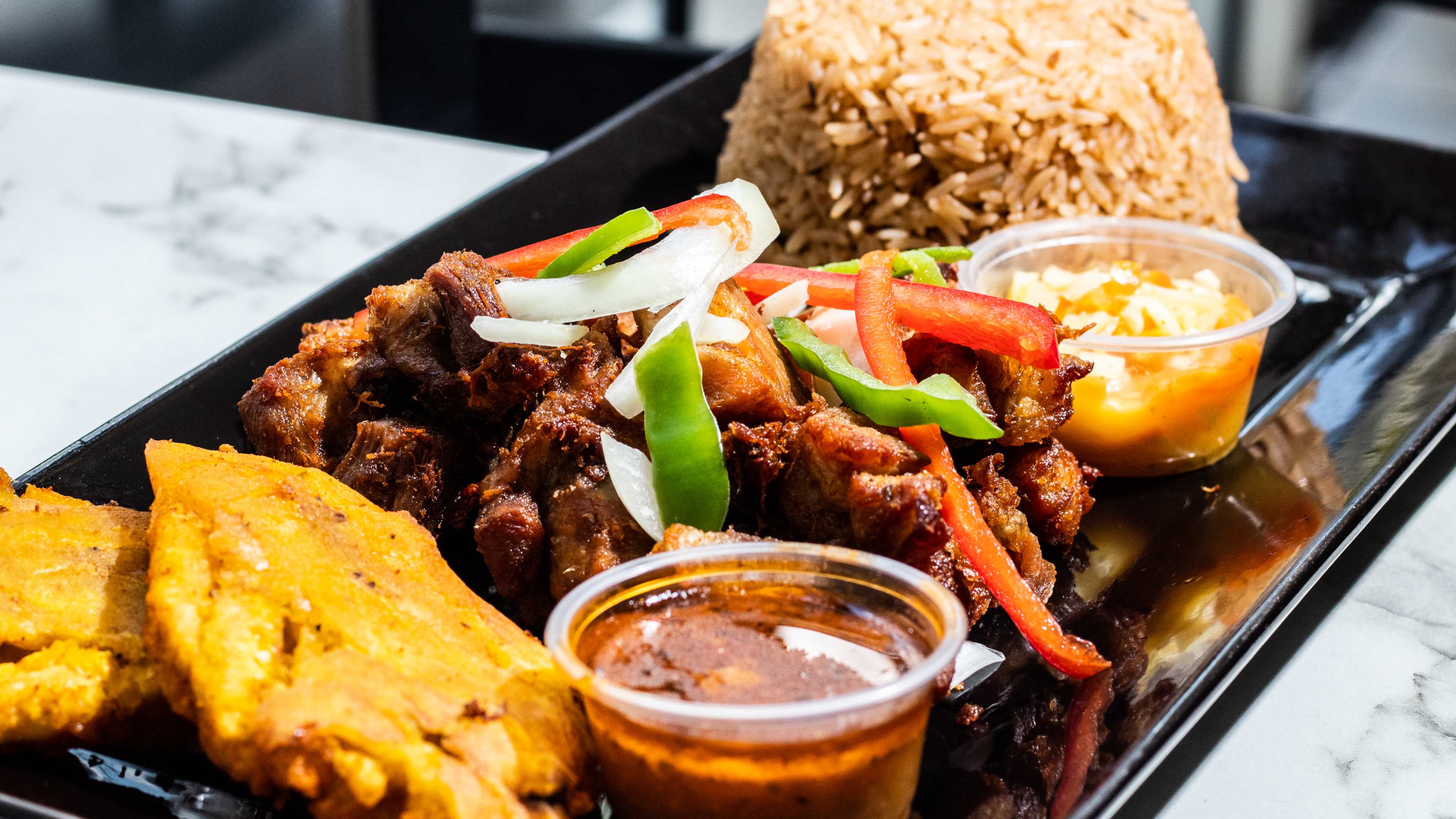Griot and a pile of rice on a rectangular black plate.