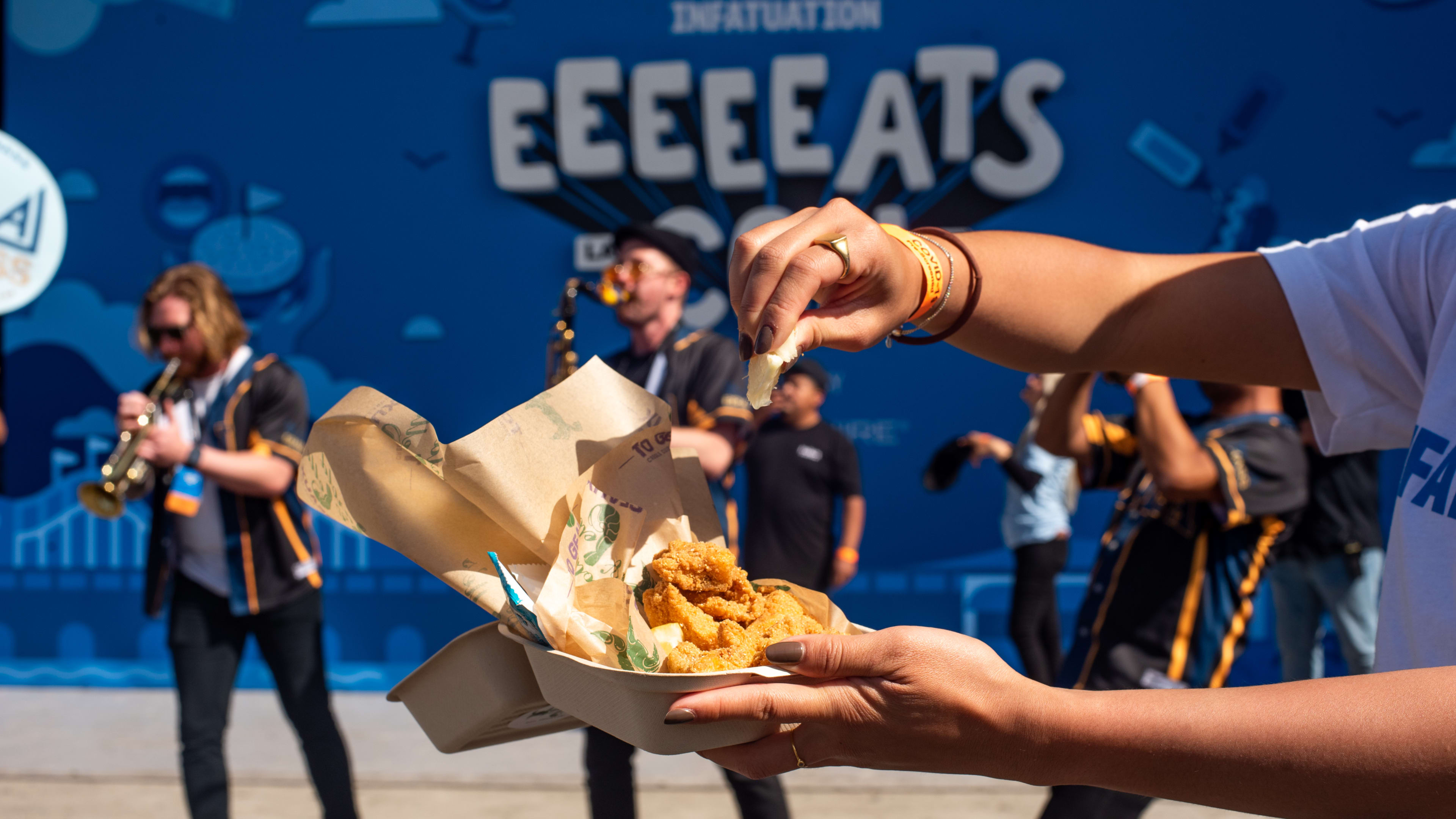 Hand holding a fry above a basket of fries in front of an Eeeeeatscon banner