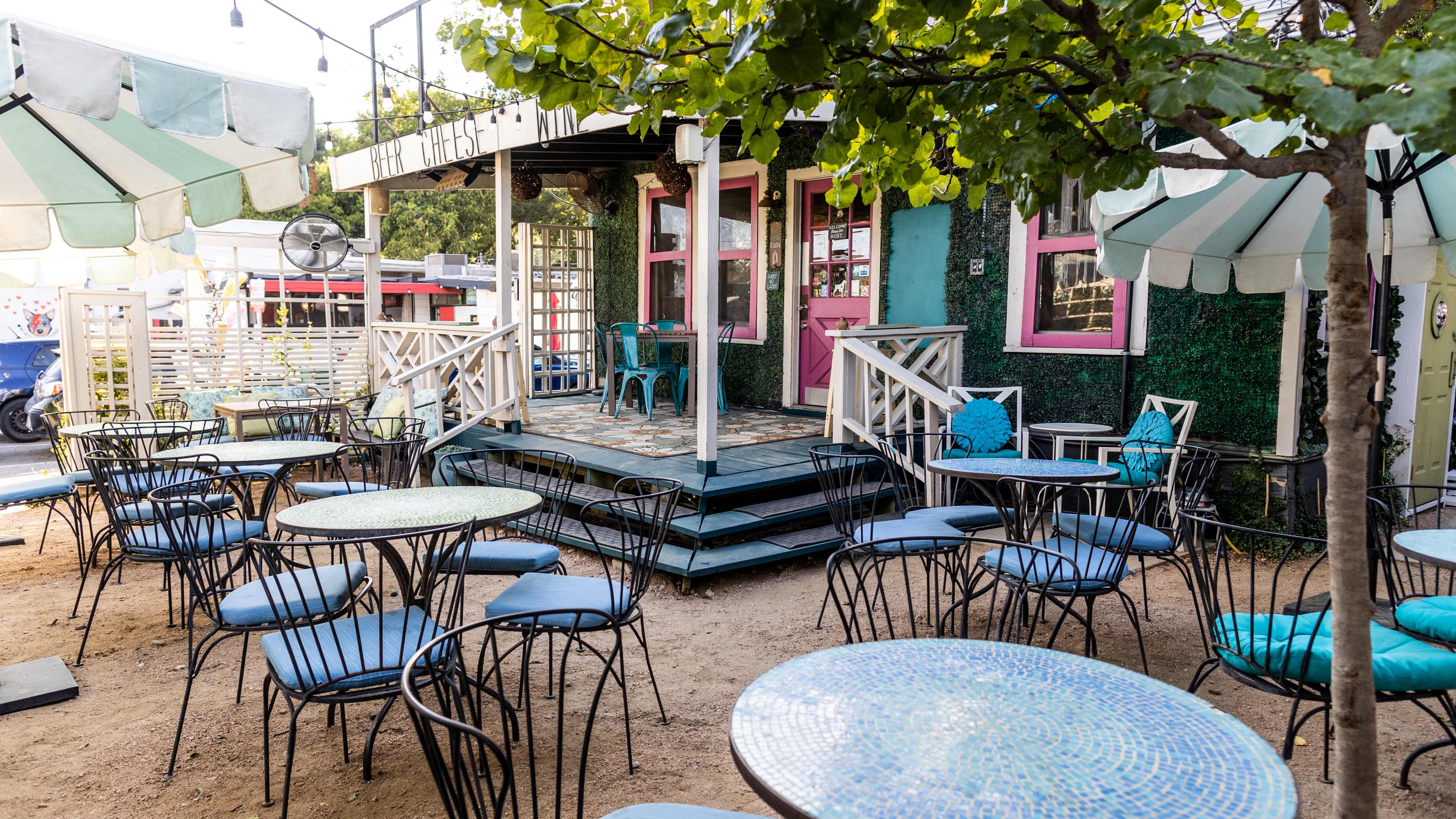 The patio at House Wine with blue and green mosaic tiled tables, blue cushioned chairs, blue and white umbrellas, and a colorfully painted building exterior.