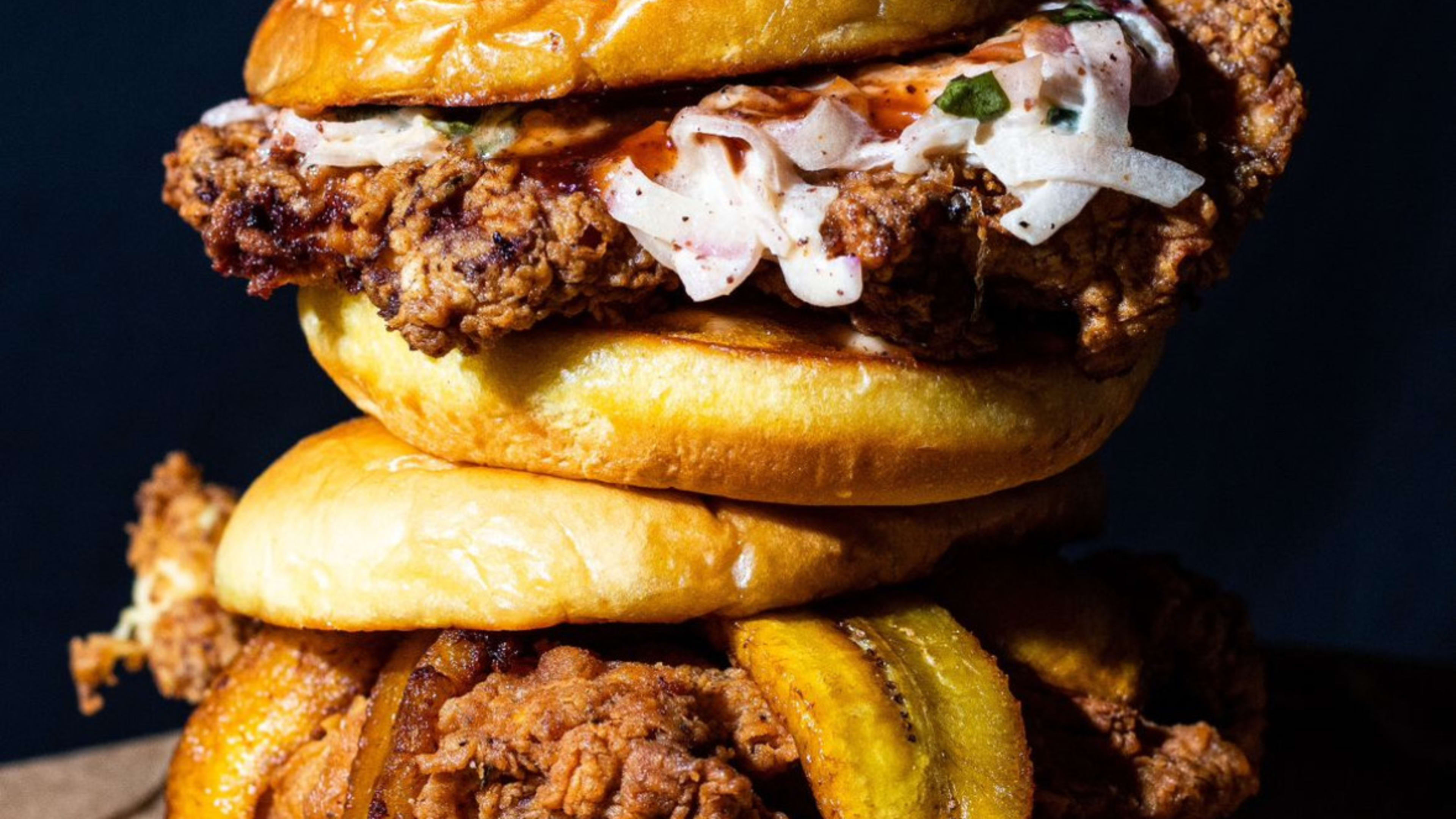 two fried chicken sandwiches stacked on top of one another.