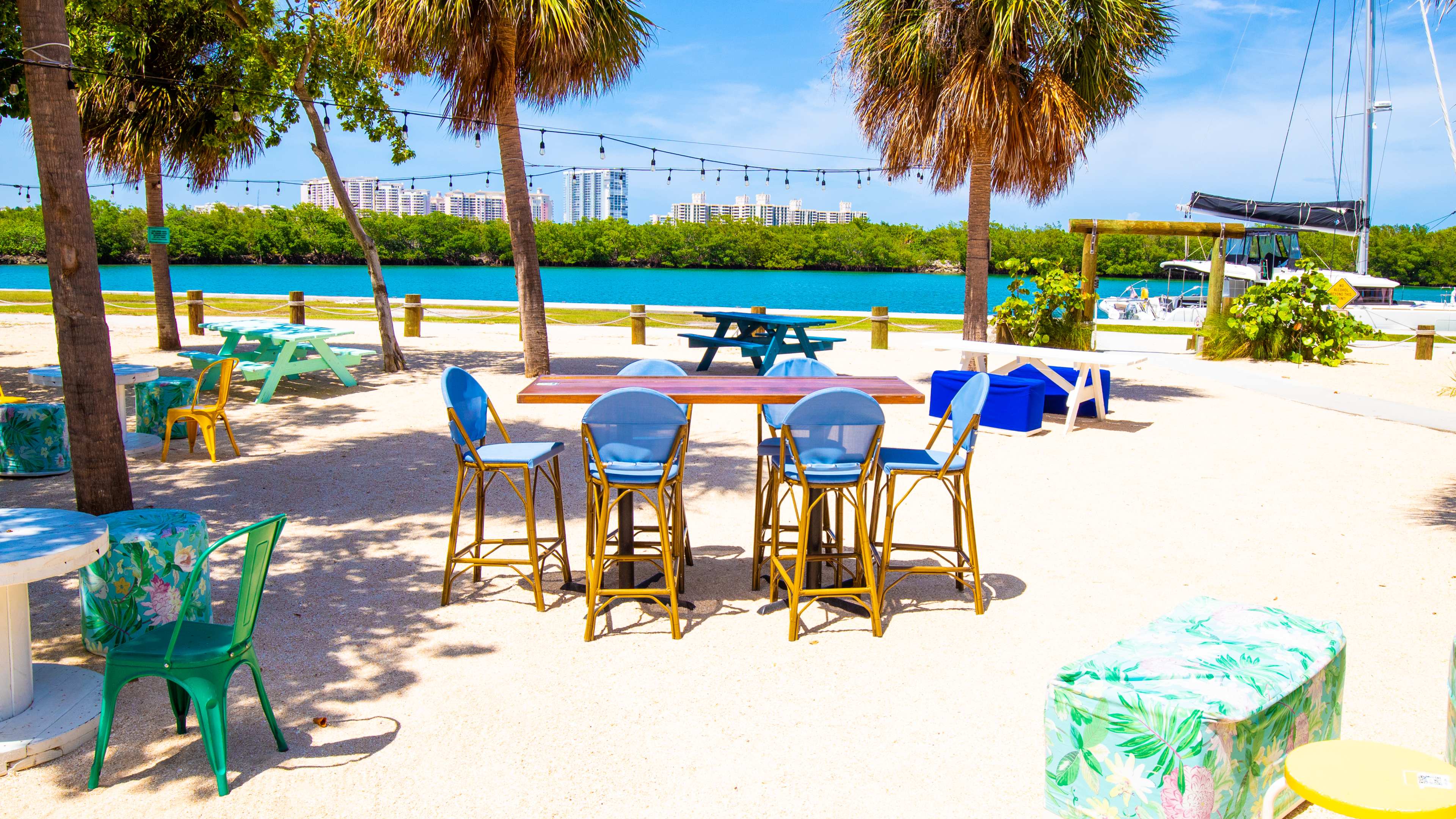 Beach patio with colorful tables and bar stools on the sand.