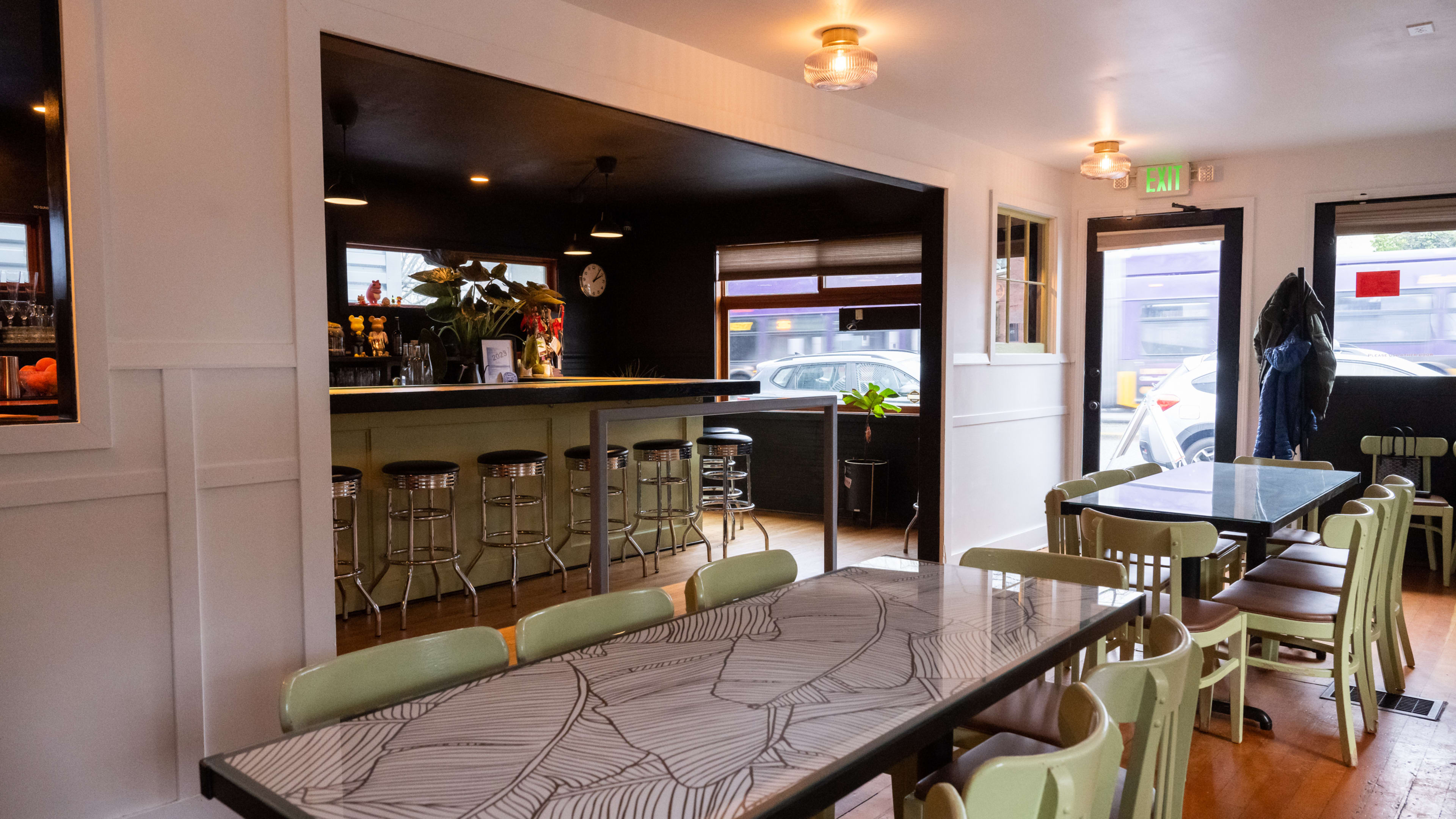 two communal tables in a dining room with a bar in the back and diner-style barstools