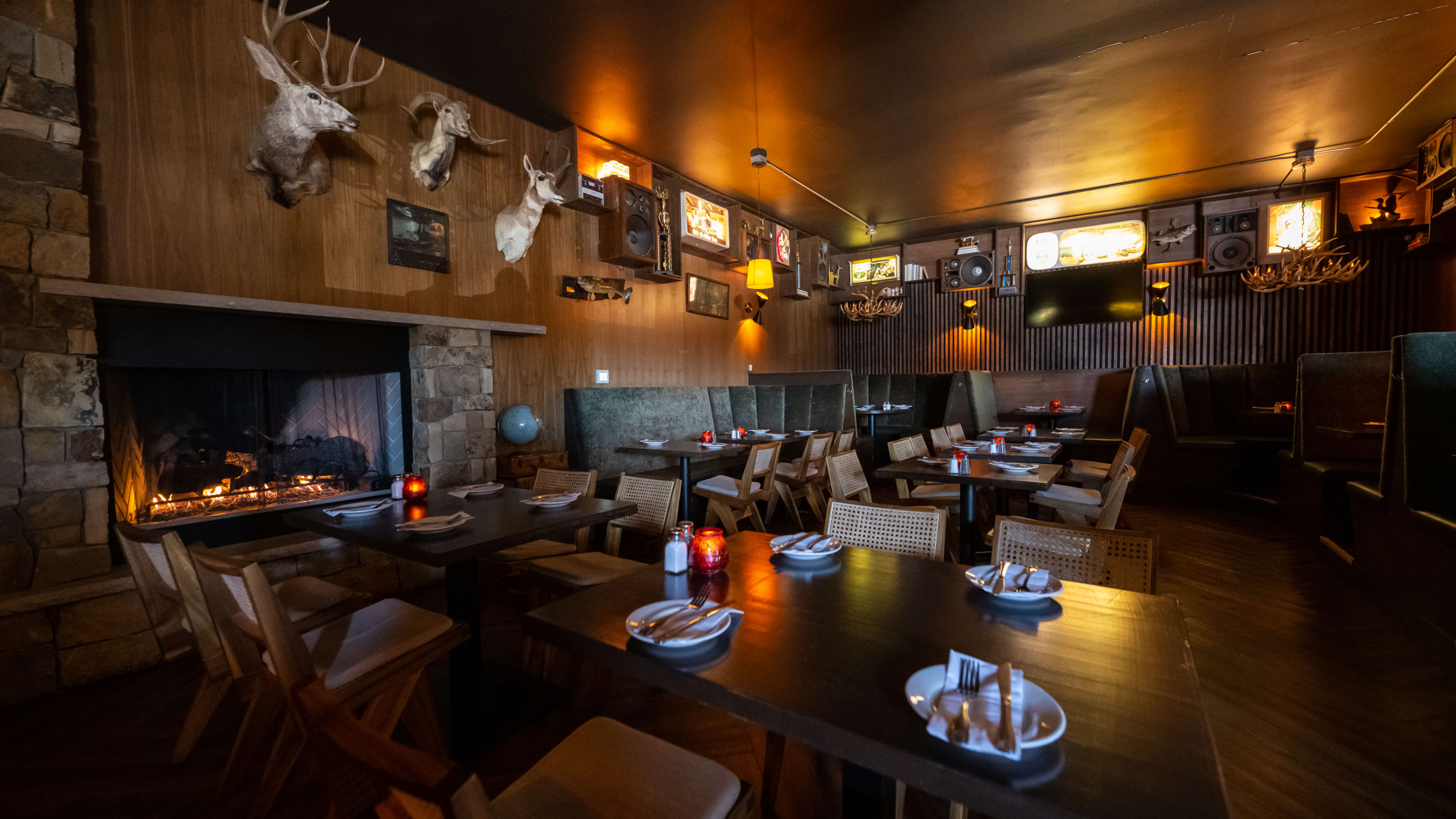 Dark cabin interior with taxidermy, a fireplace, and leather booths.