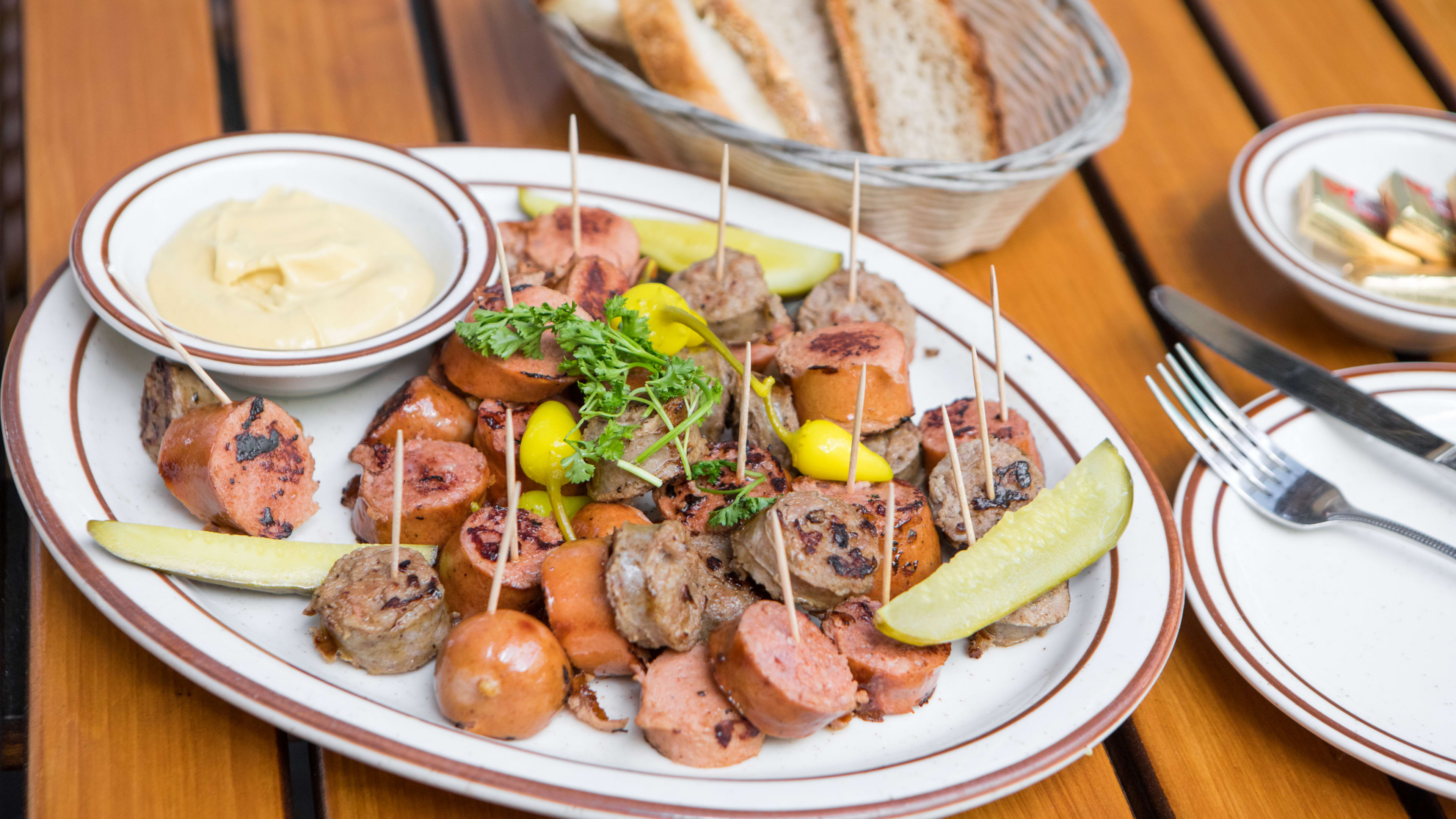 A plate of the sausage sampler on a wood slat table with a basket of bread on the side.