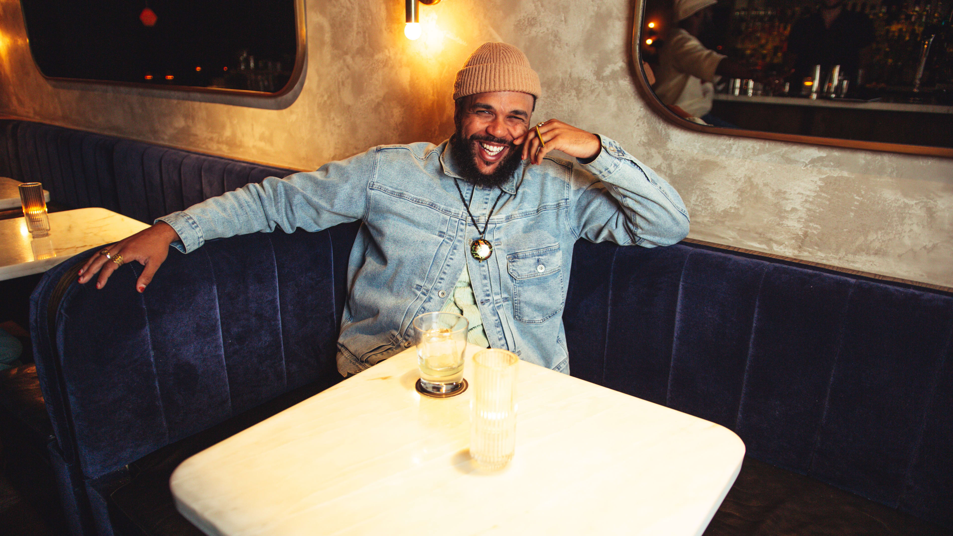 Musician Jidenna sitting in a velvet booth at Death & Co in LA