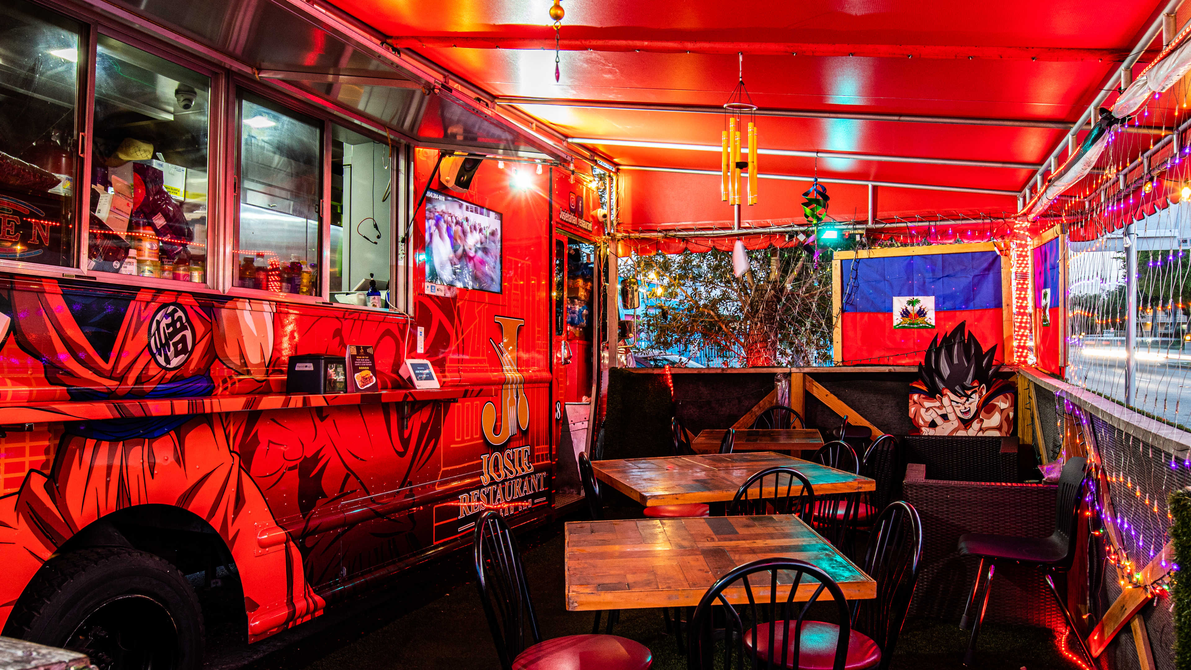 A red food truck with some chairs and an awning in front of it.