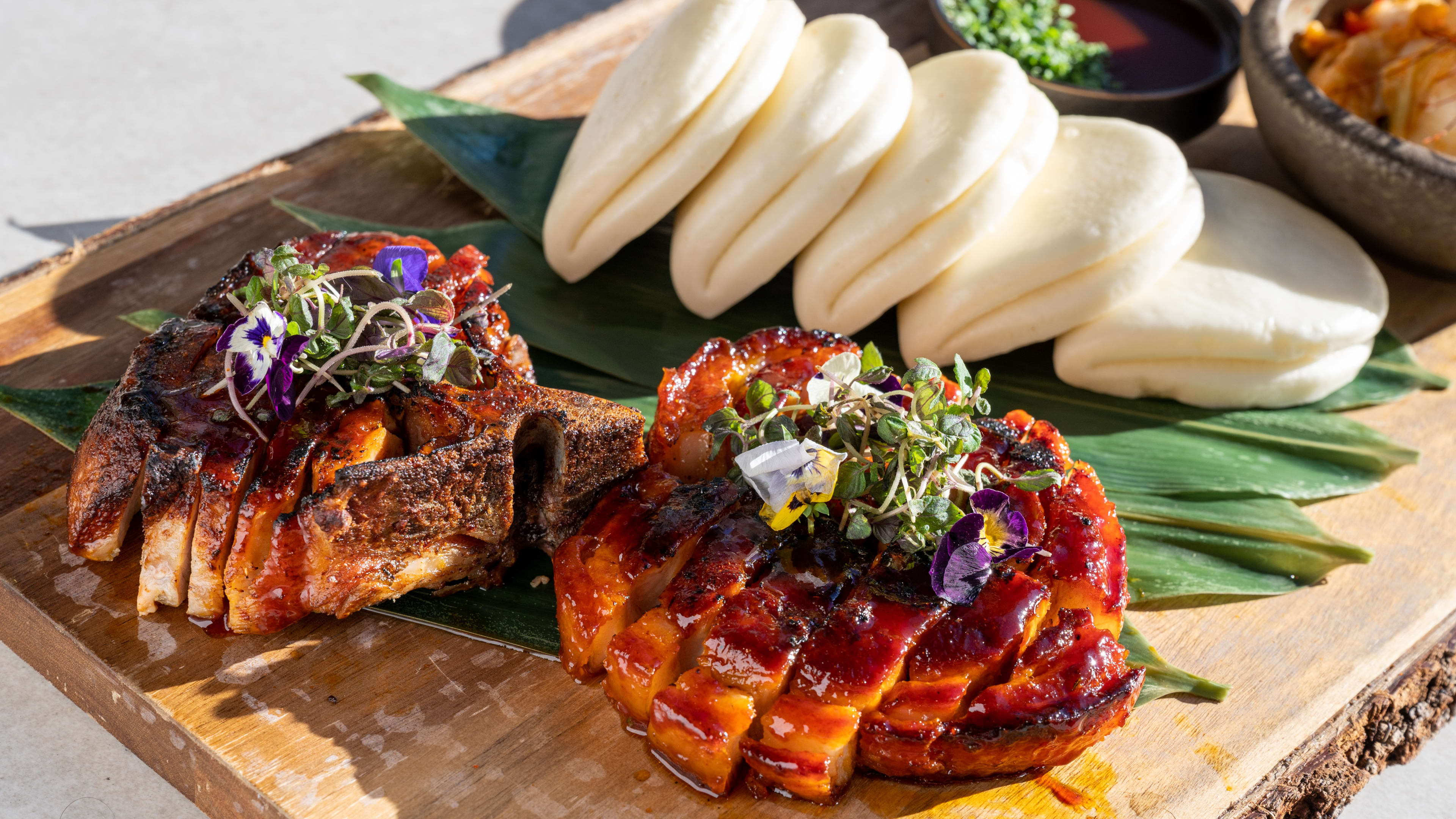 Sliced pork with bao buns on a wooden platter.