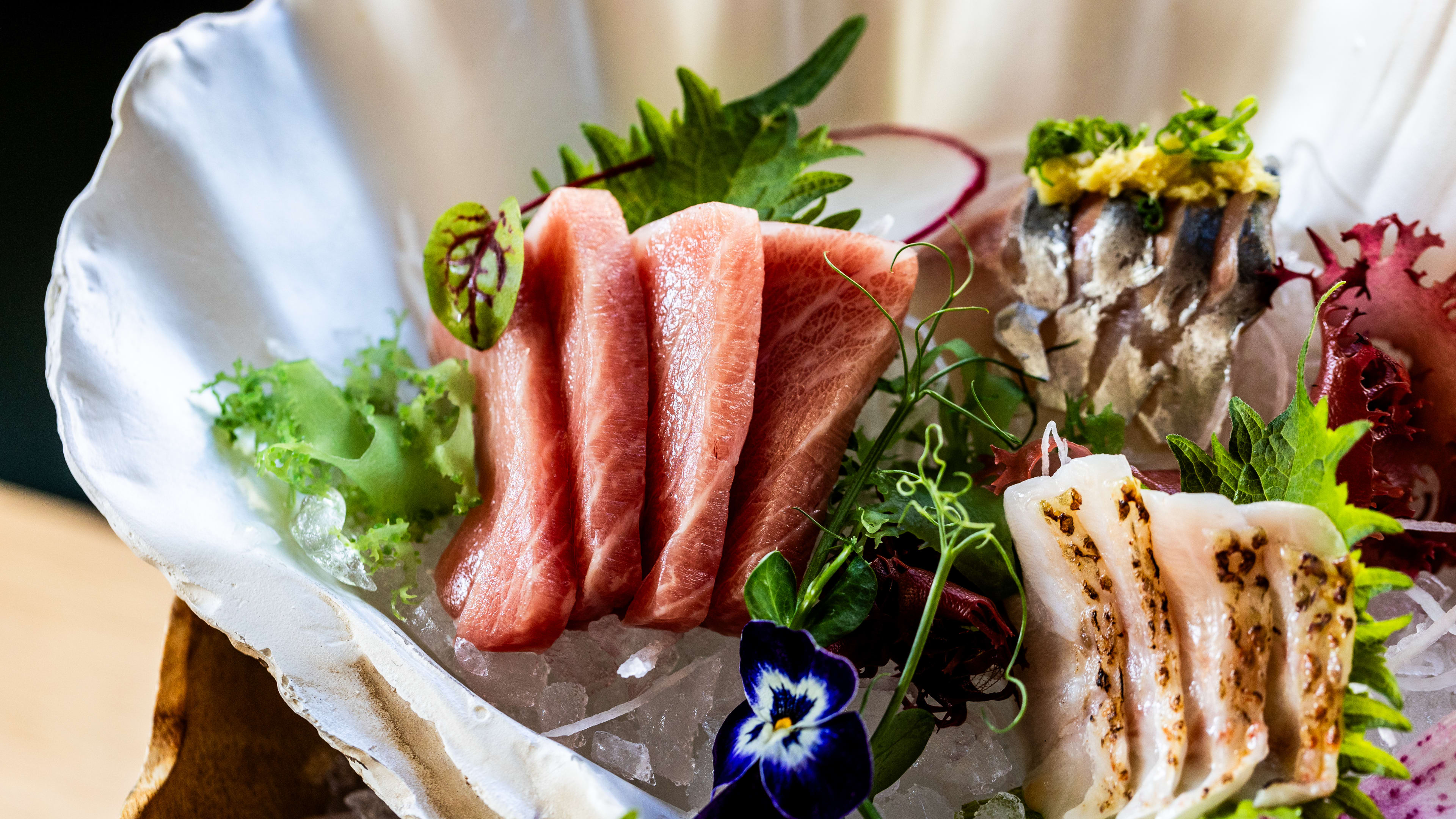 close up of Katami sashimi inside of a white shell plate surrounded by edible flowers