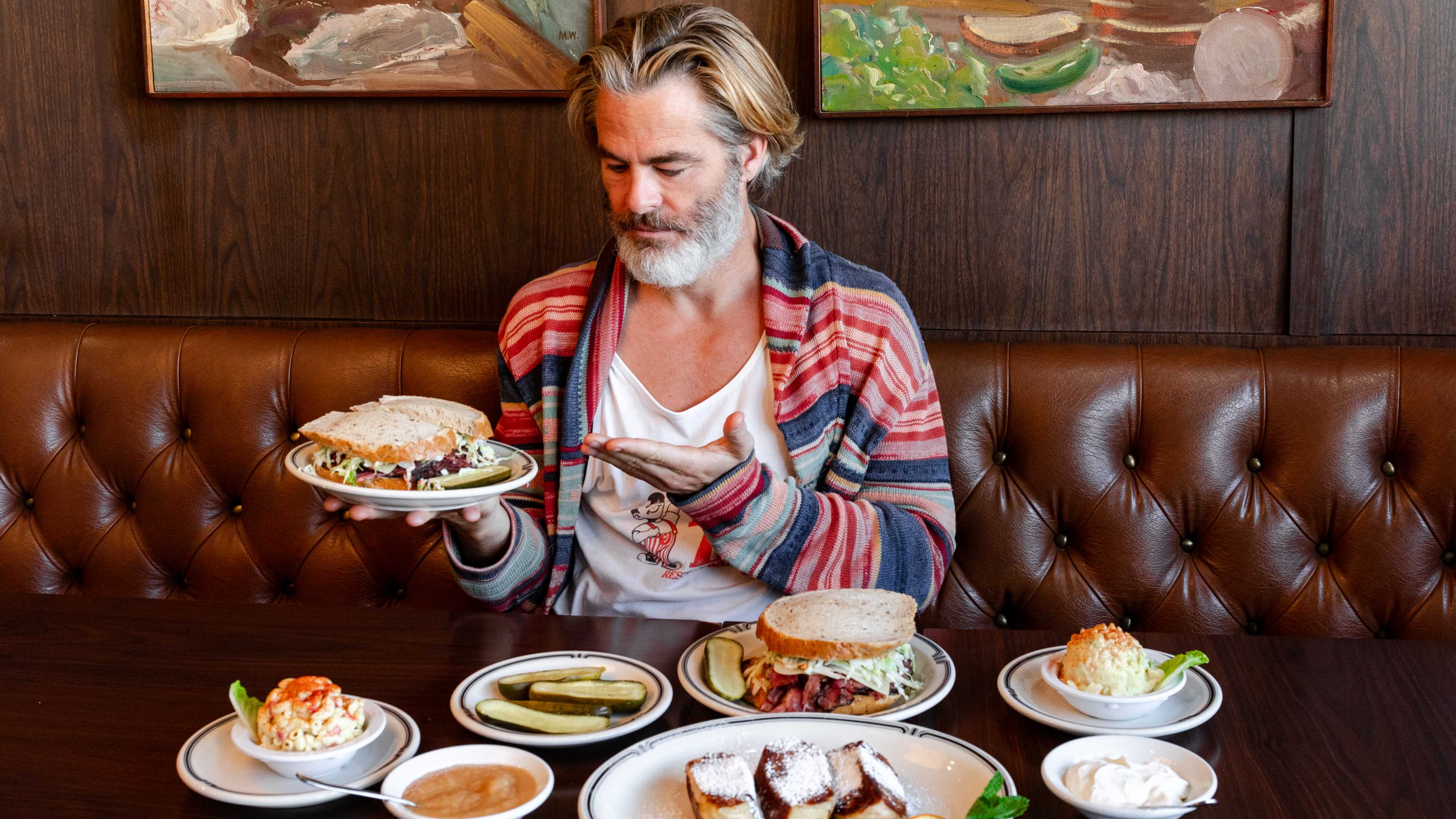 the actor chris pine holds up a sandwich on a plate