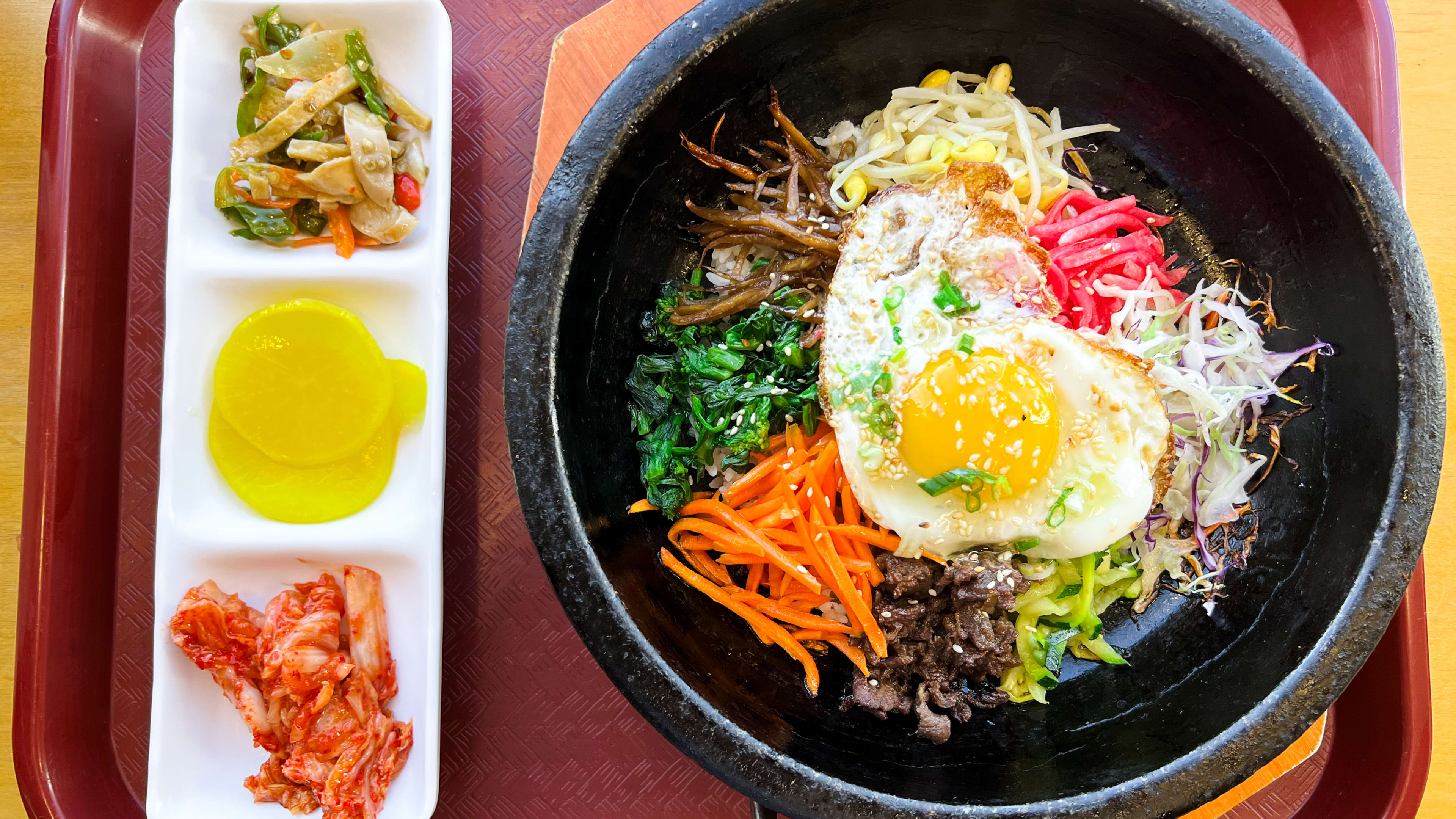 A bowl of bibimbap and accompanying sides on a red lunch tray.