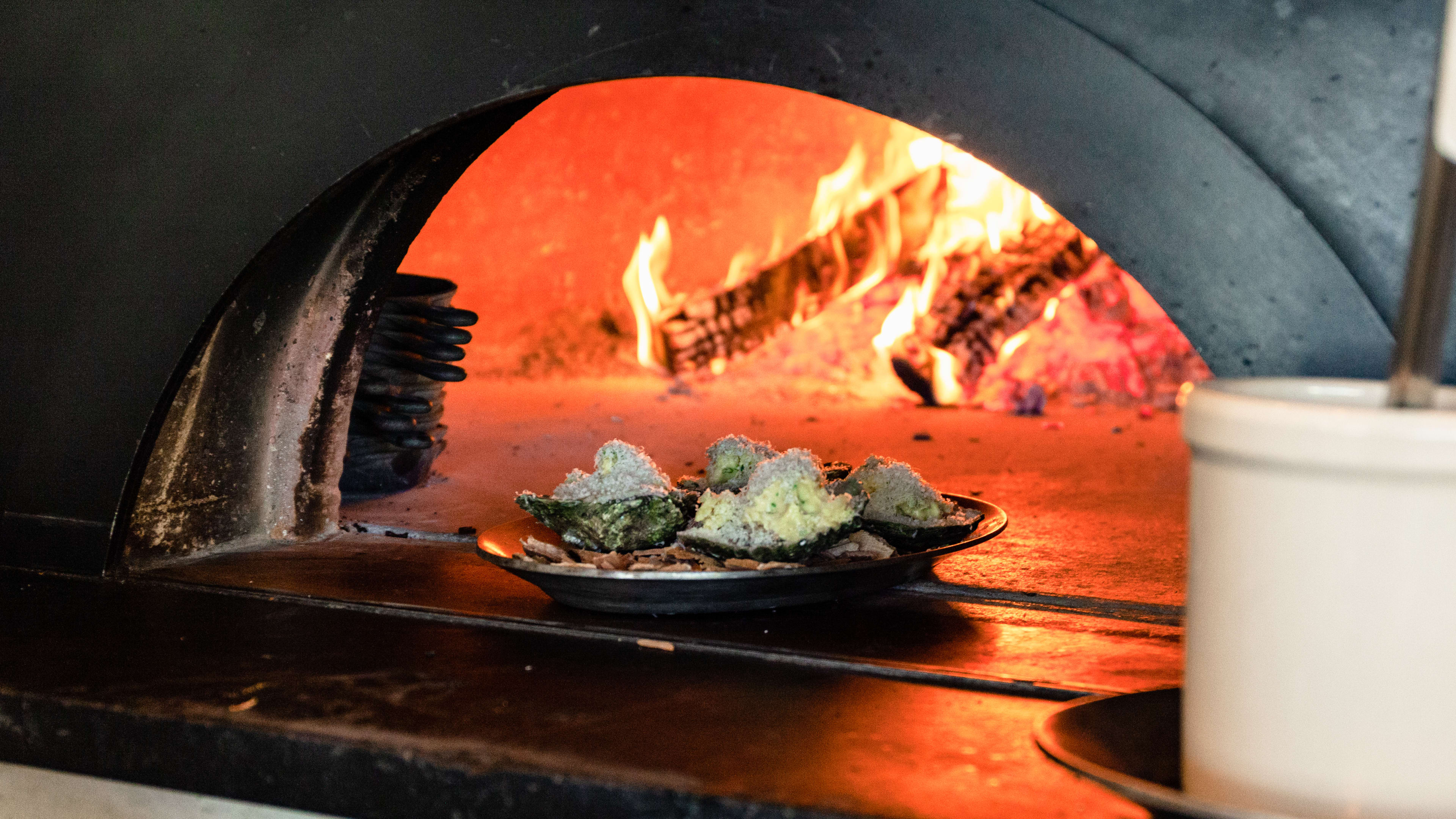 Wood roasted oysters on a plate in front of the live hearth oven.