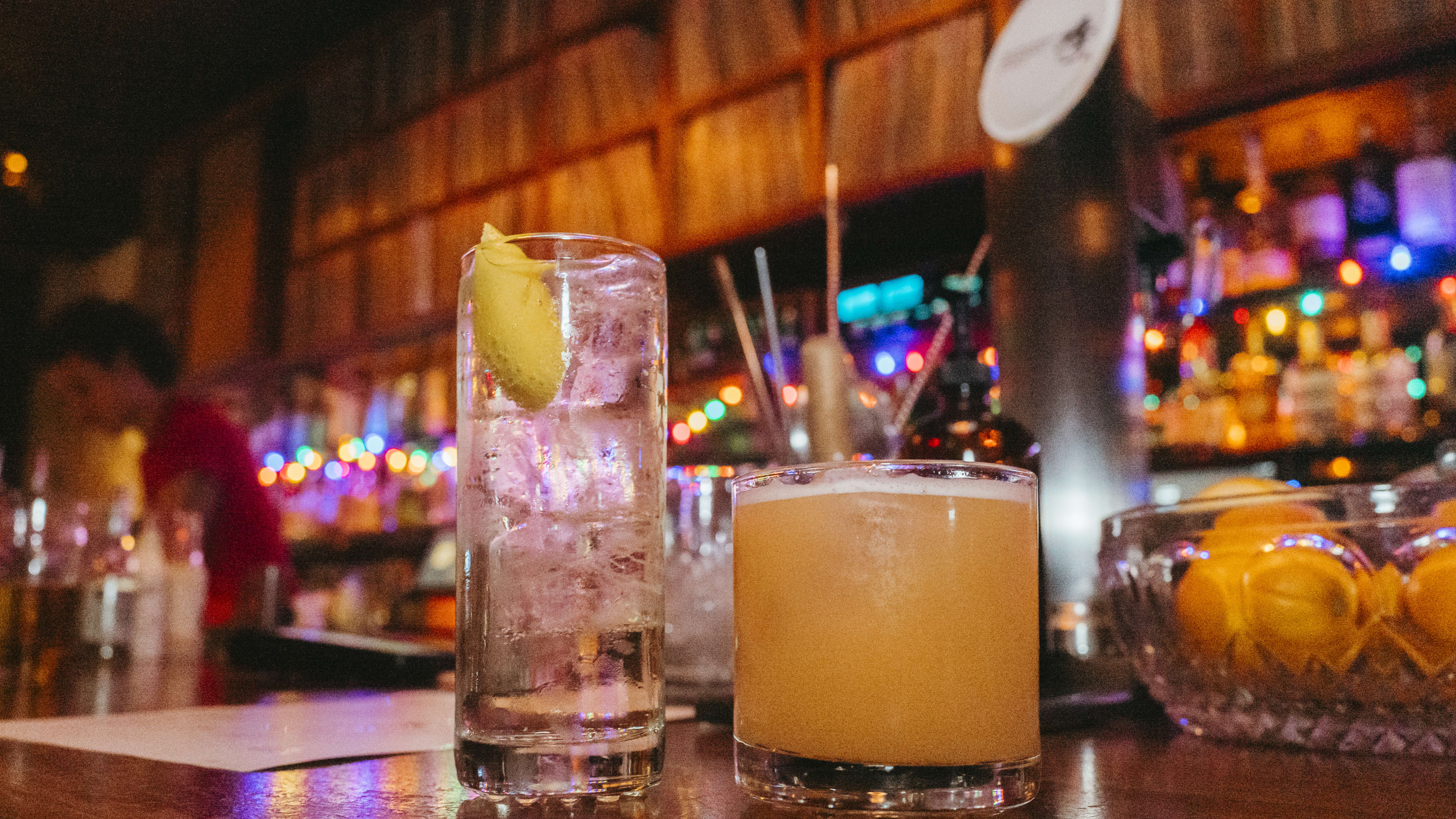 Two cocktails on a wooden bar. Vinyl records line built-ins on the back wall.