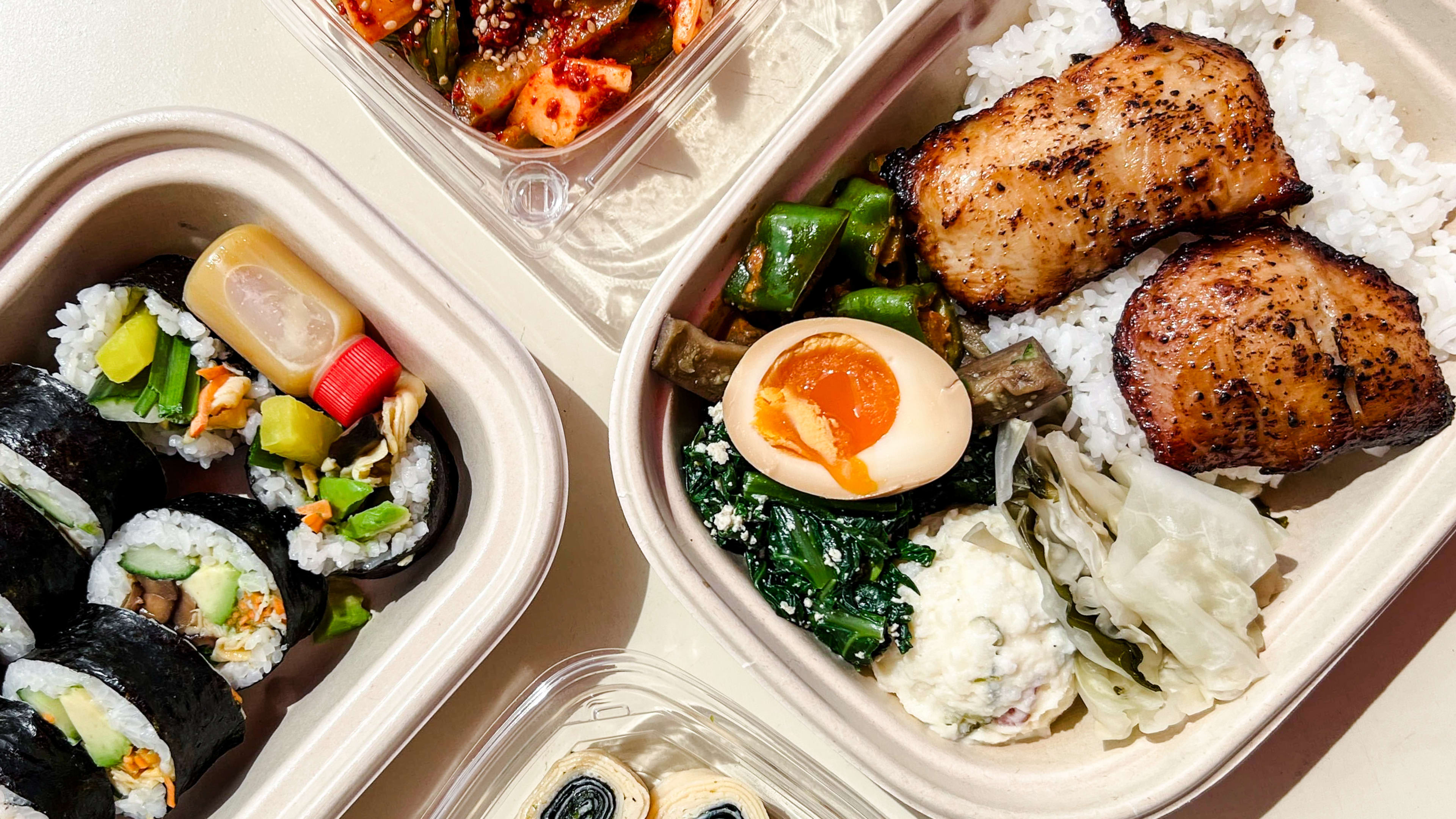 A spread of takeaway containers with sushi, meat and veggies.