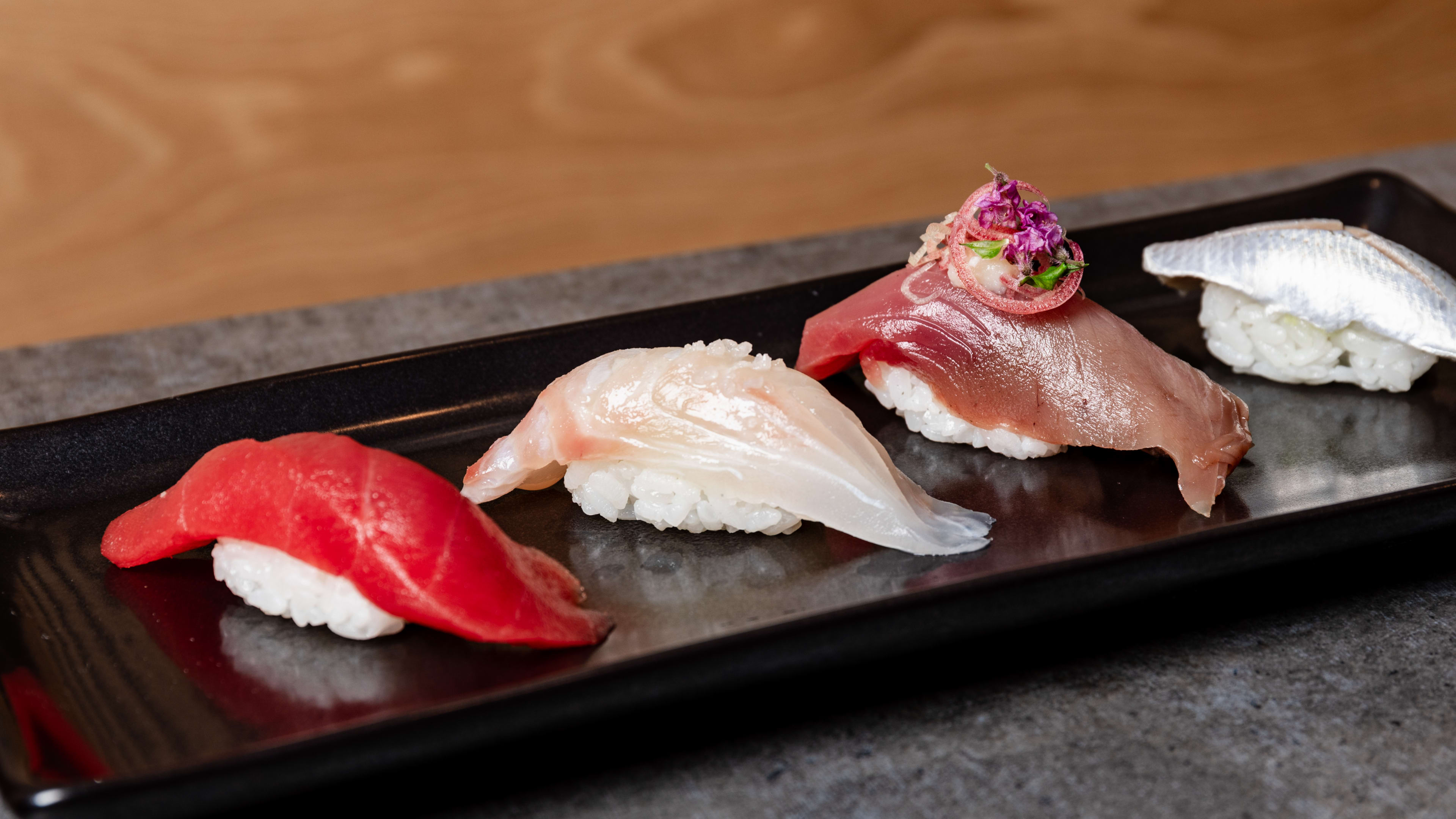 Four pieces of nigiri on a black slate platter.