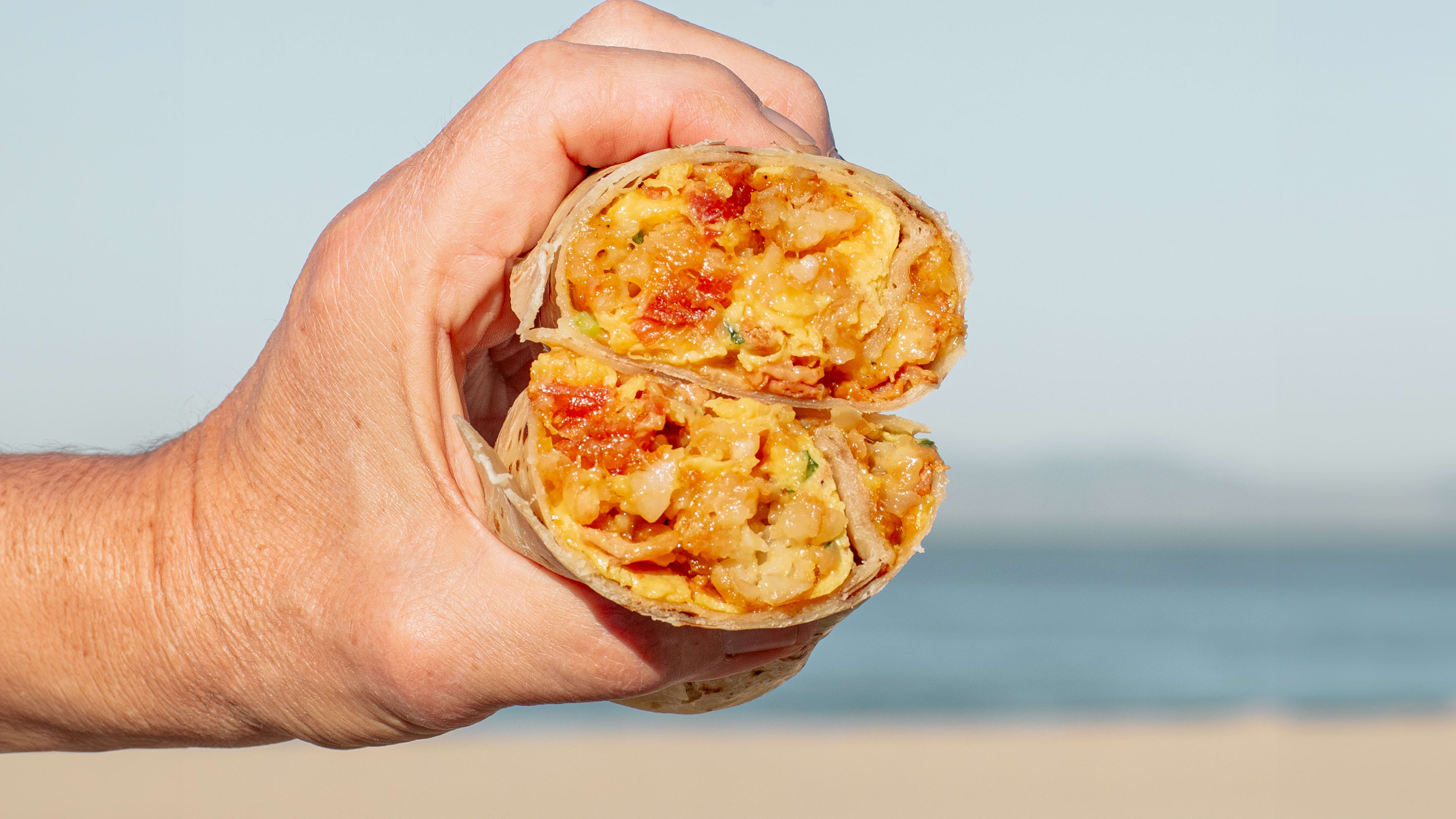 A cross section of a burrito held up against the ocean skyline.