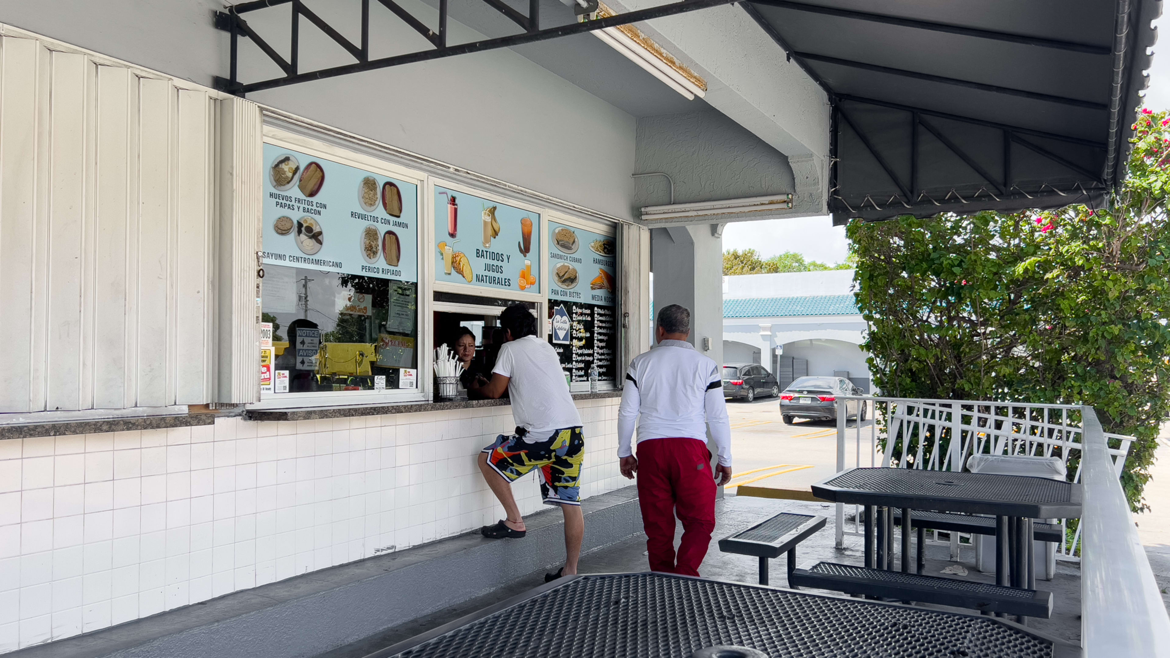 An outdoor window where you can order food from and two black tables.