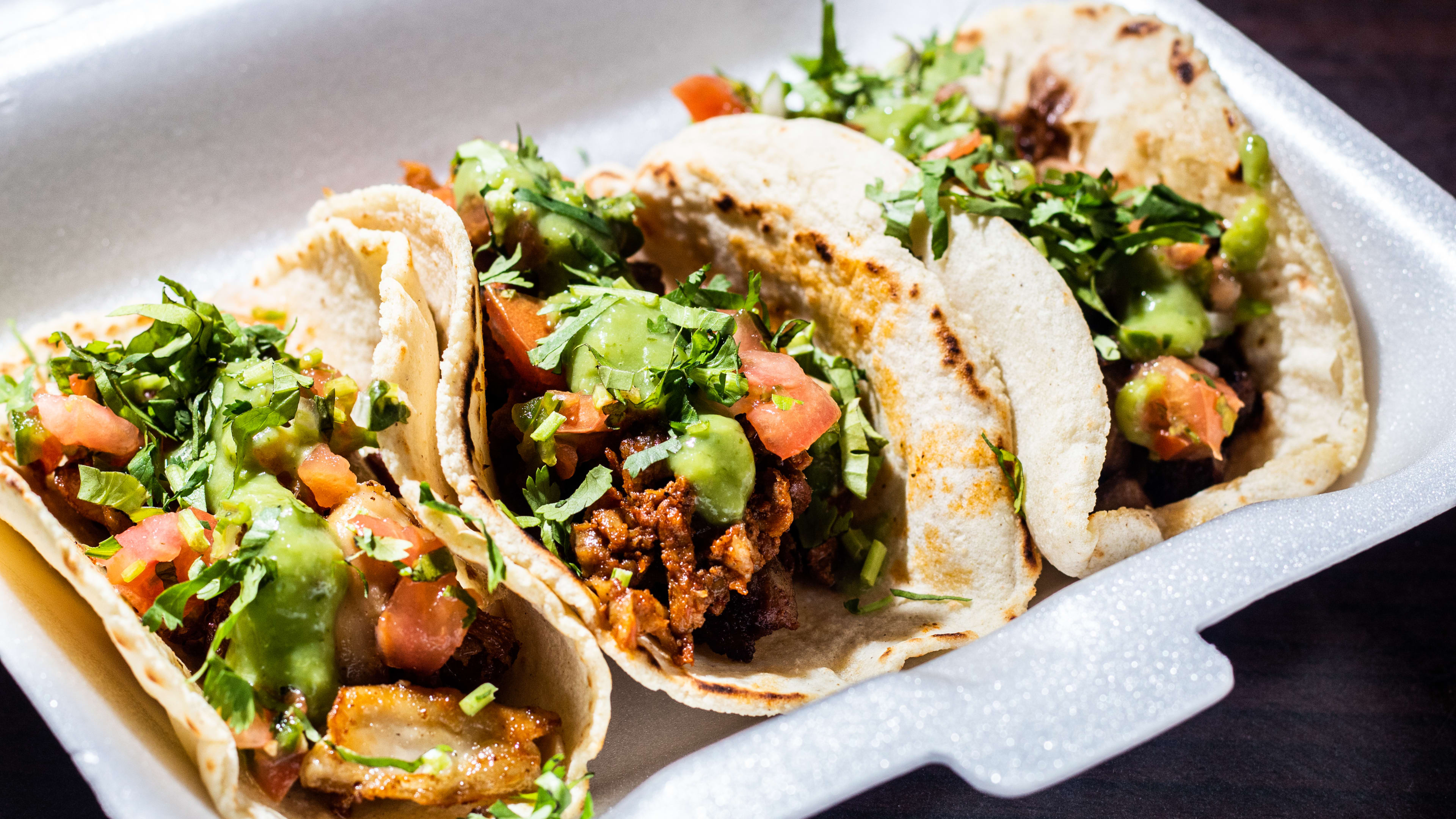 Three tripe tacos with guacamole, pico de gallo, and cilantro in a takeout box.