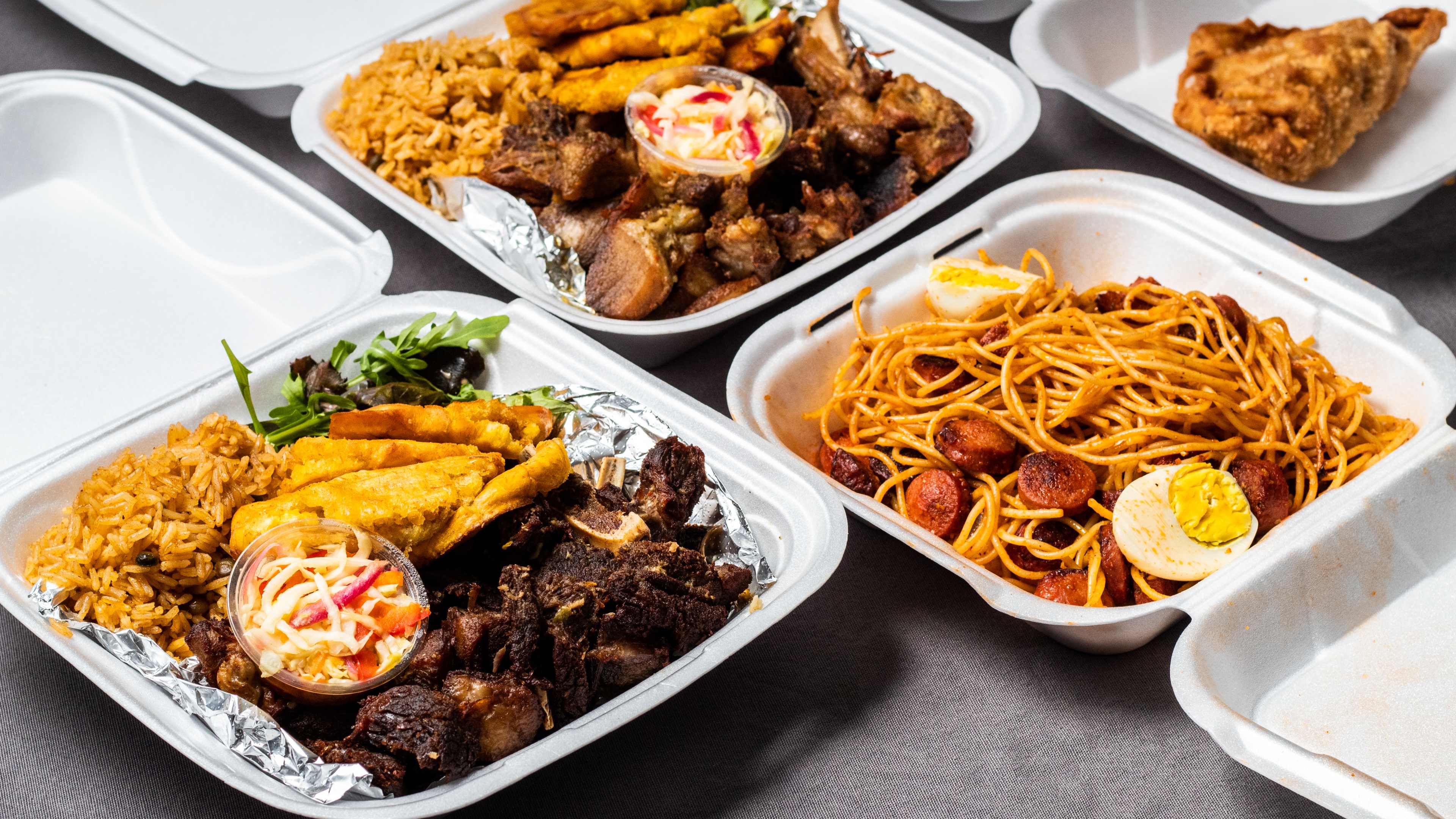 Takeout boxes full of Haitian dishes, including fried goat, spaghetti, and more.