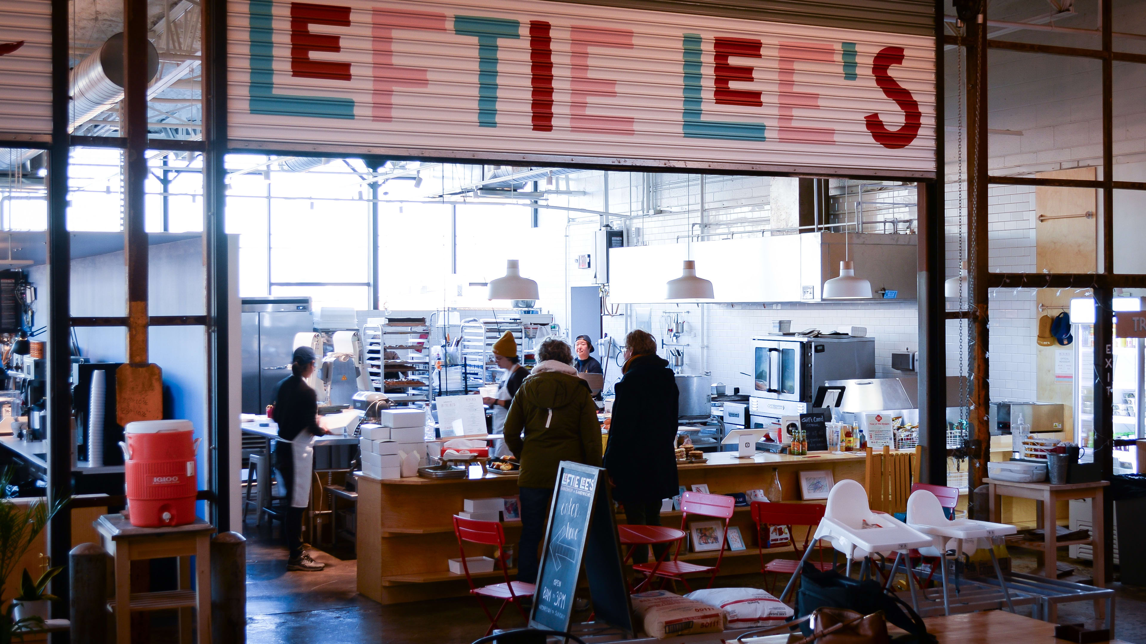 Interior of food hall bakery with colorful sign and ordering counter with bakery production visible in back.