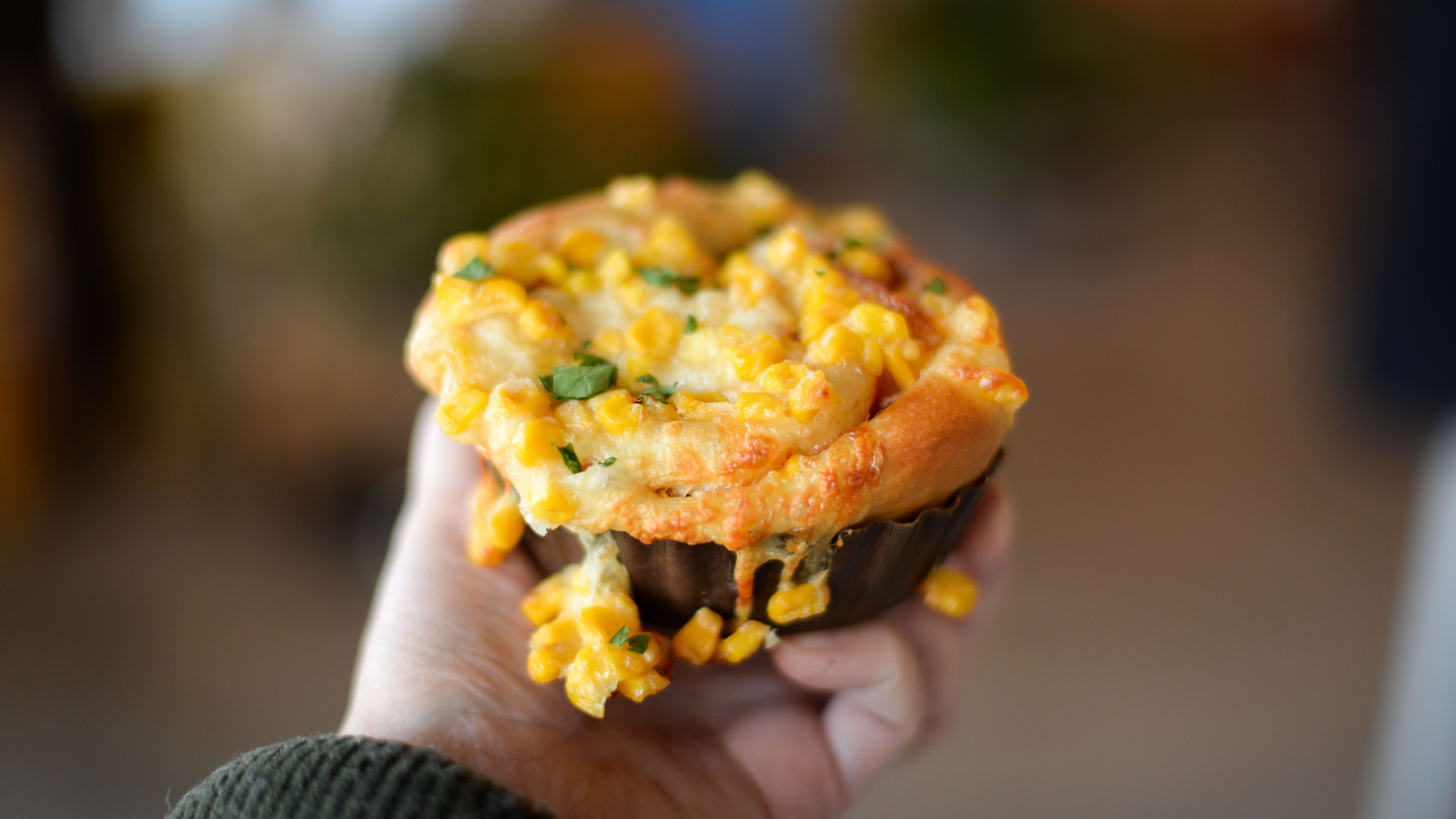 Hand holding bread bun topped with corn and melty cheese.