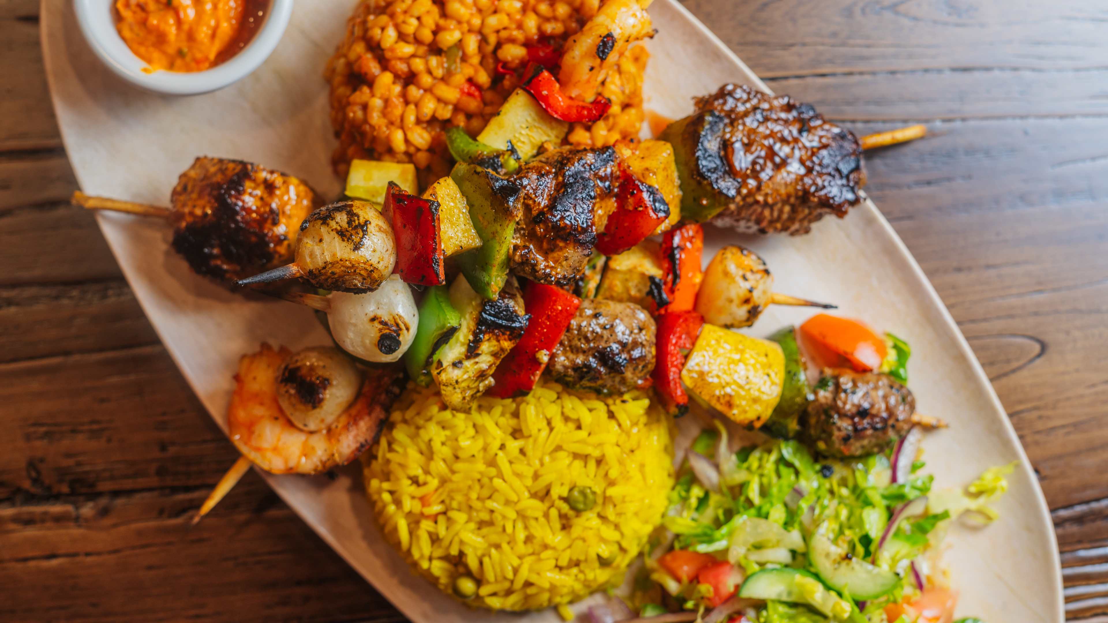 Plate with piles of salad, rice, and couscous topped with three grilled kabob skewers