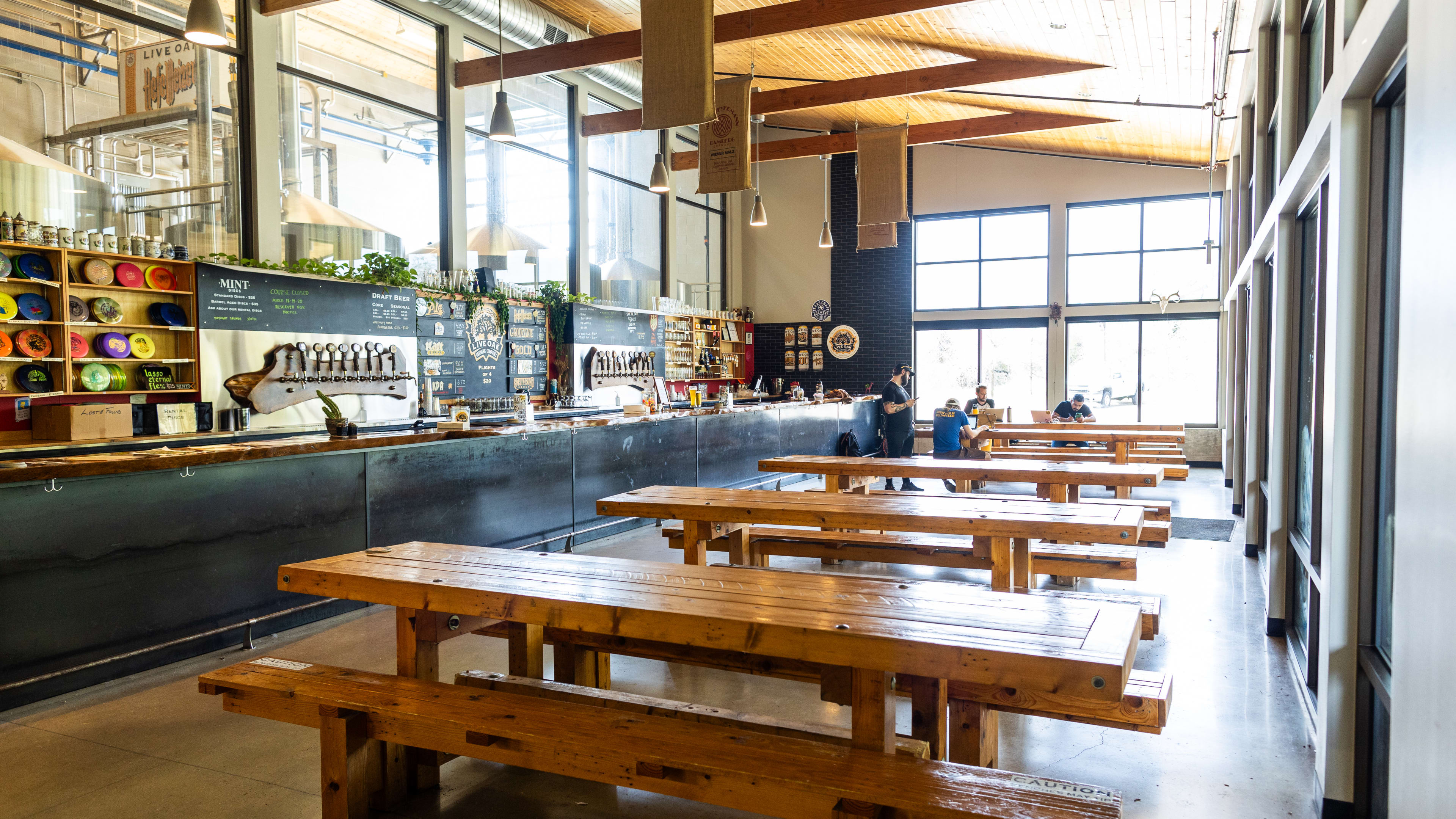 The spacious interior of Live Oak lined with wooden picnic style tables, and a long bar.