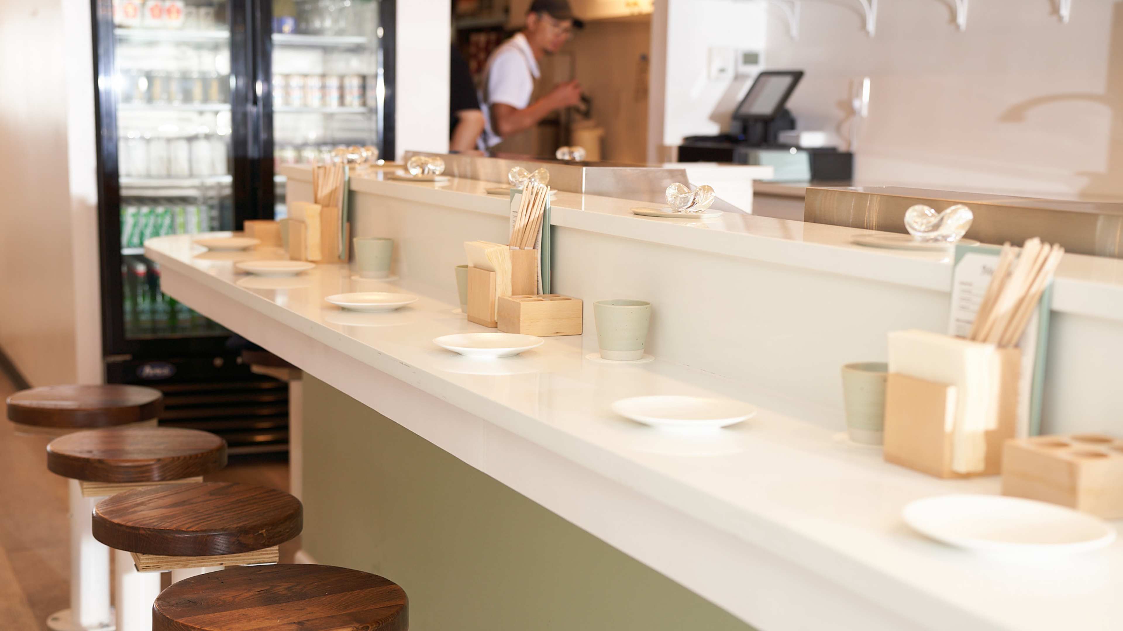 A restaurant counter with a few stools in front of it.