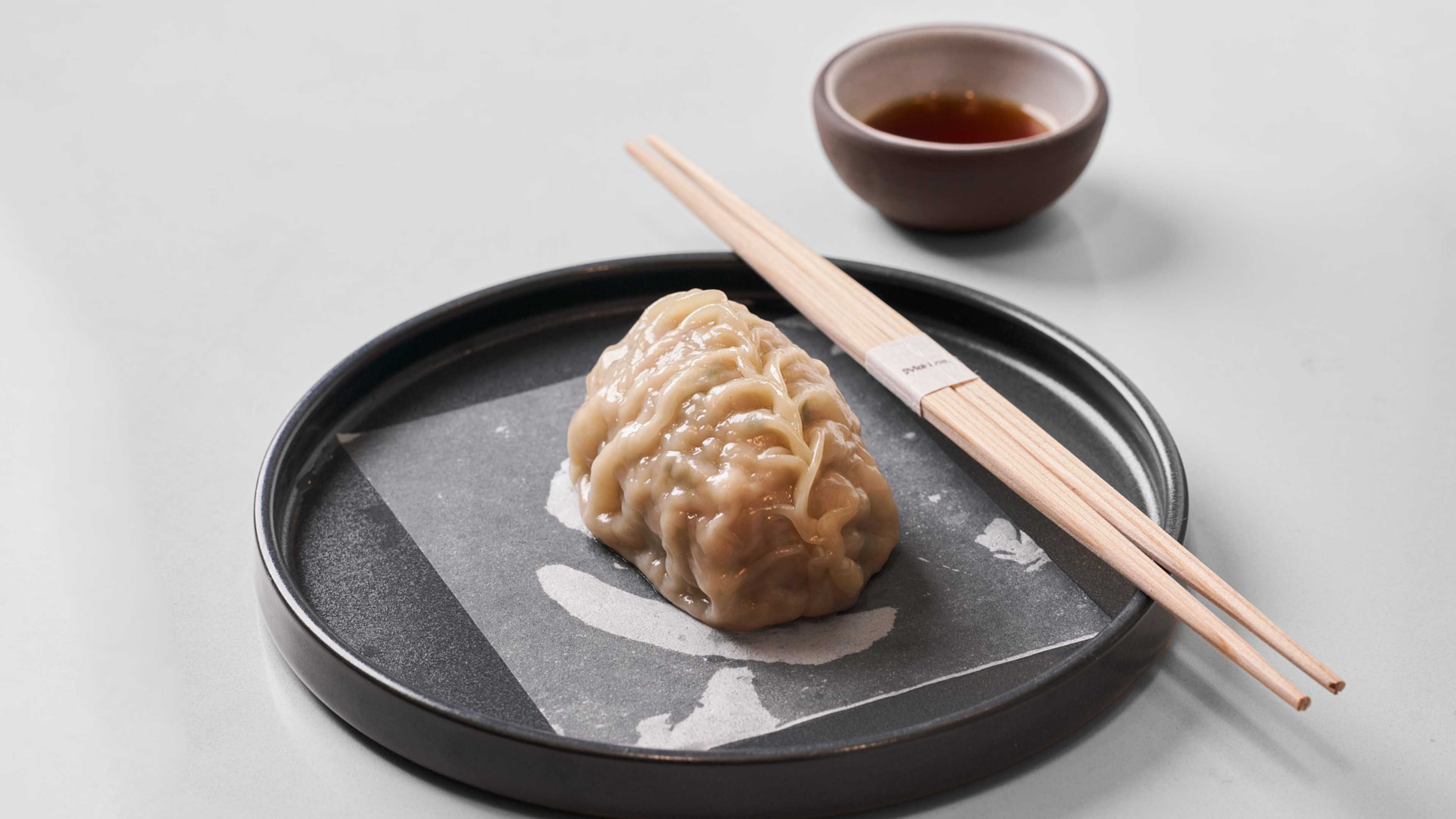 A big dumpling on a plate with chopsticks on the side.