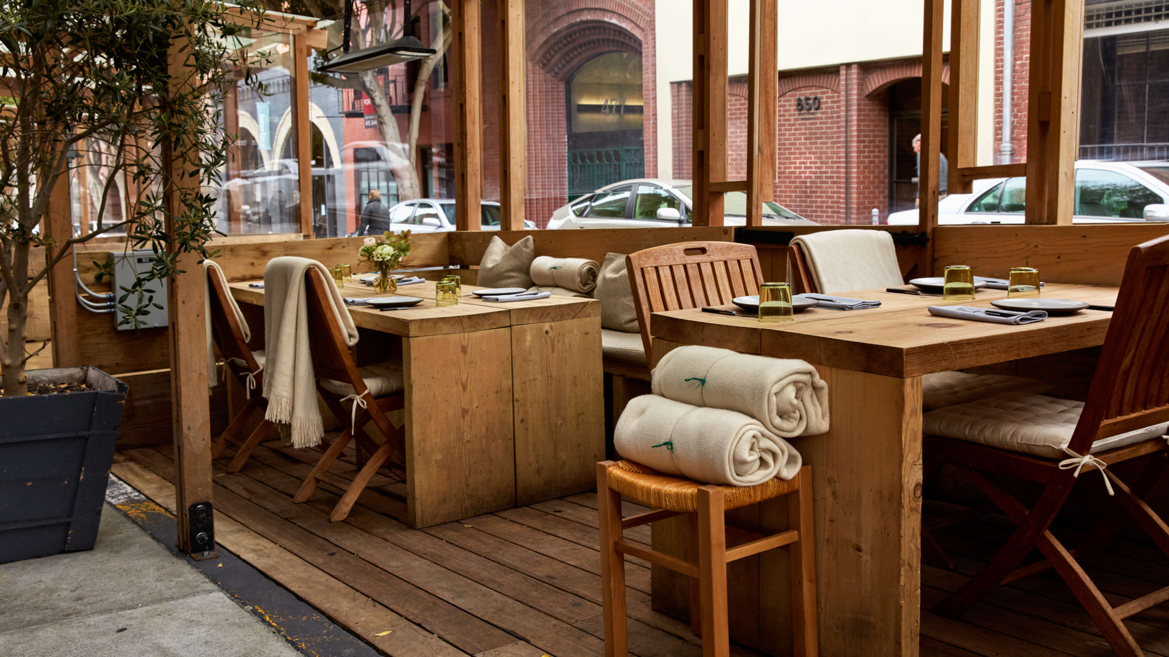 outdoor parklet with wooden tables and chairs and blankets rolled up on side tables.