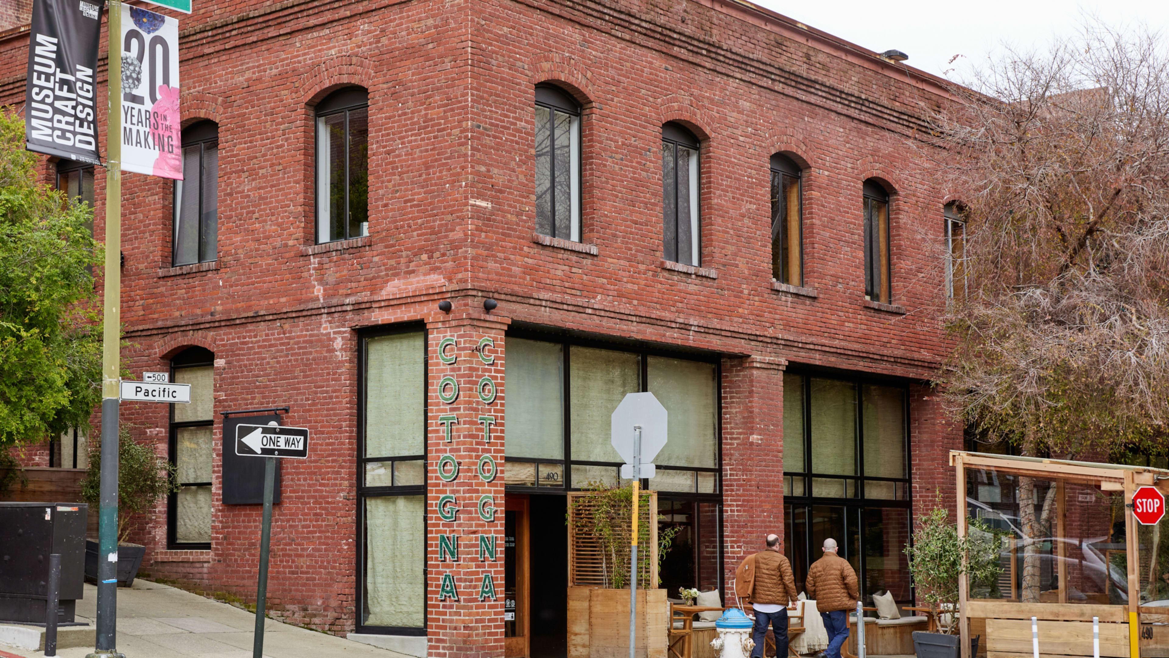 brick exterior of restaurant on tree-lined street corner with cotogna painted vertically on column next to parklet