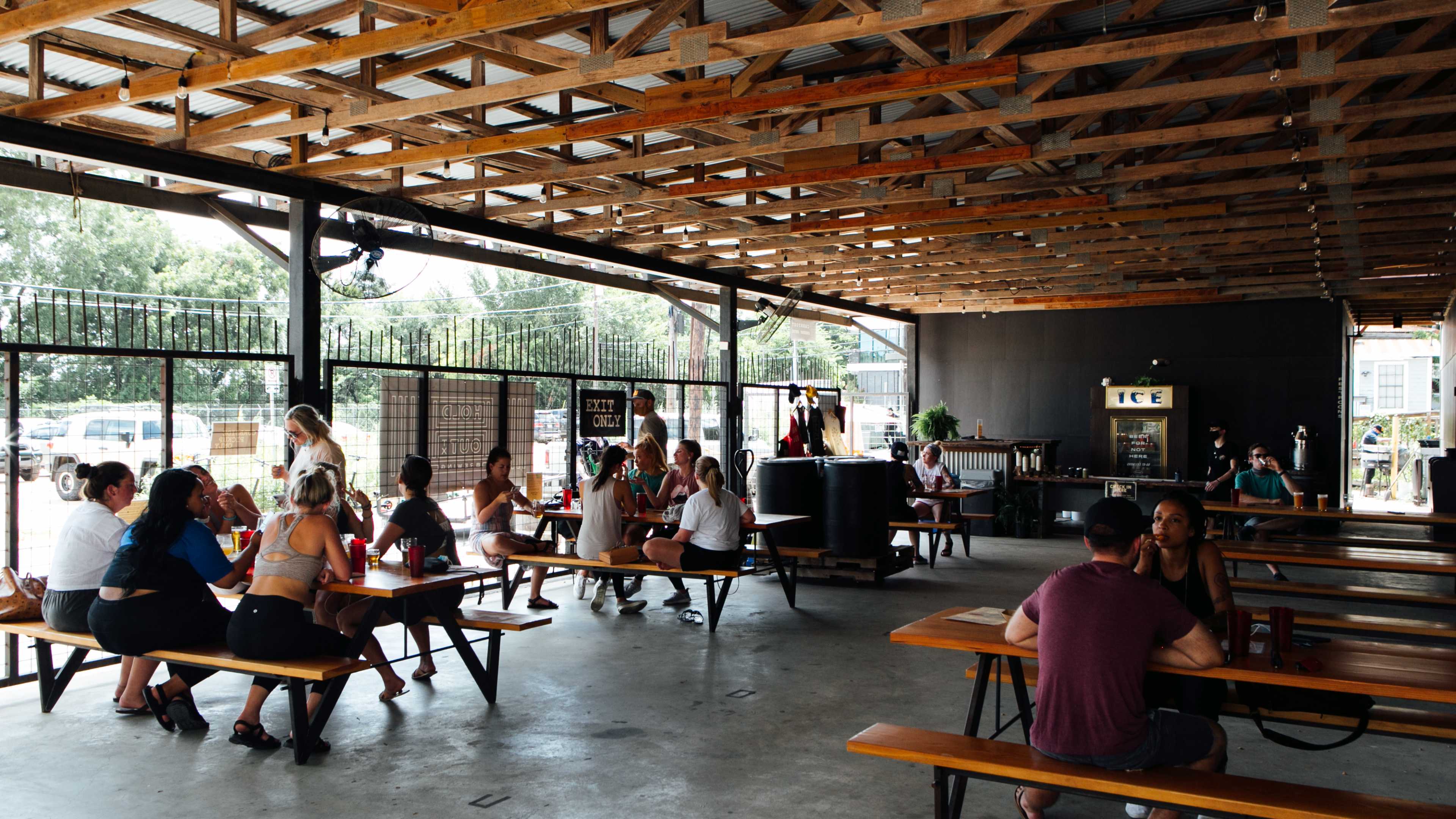 The open air beer interior Hold Out.  There are long picnic style tables, concrete floors and exposed beams on the ceiling.