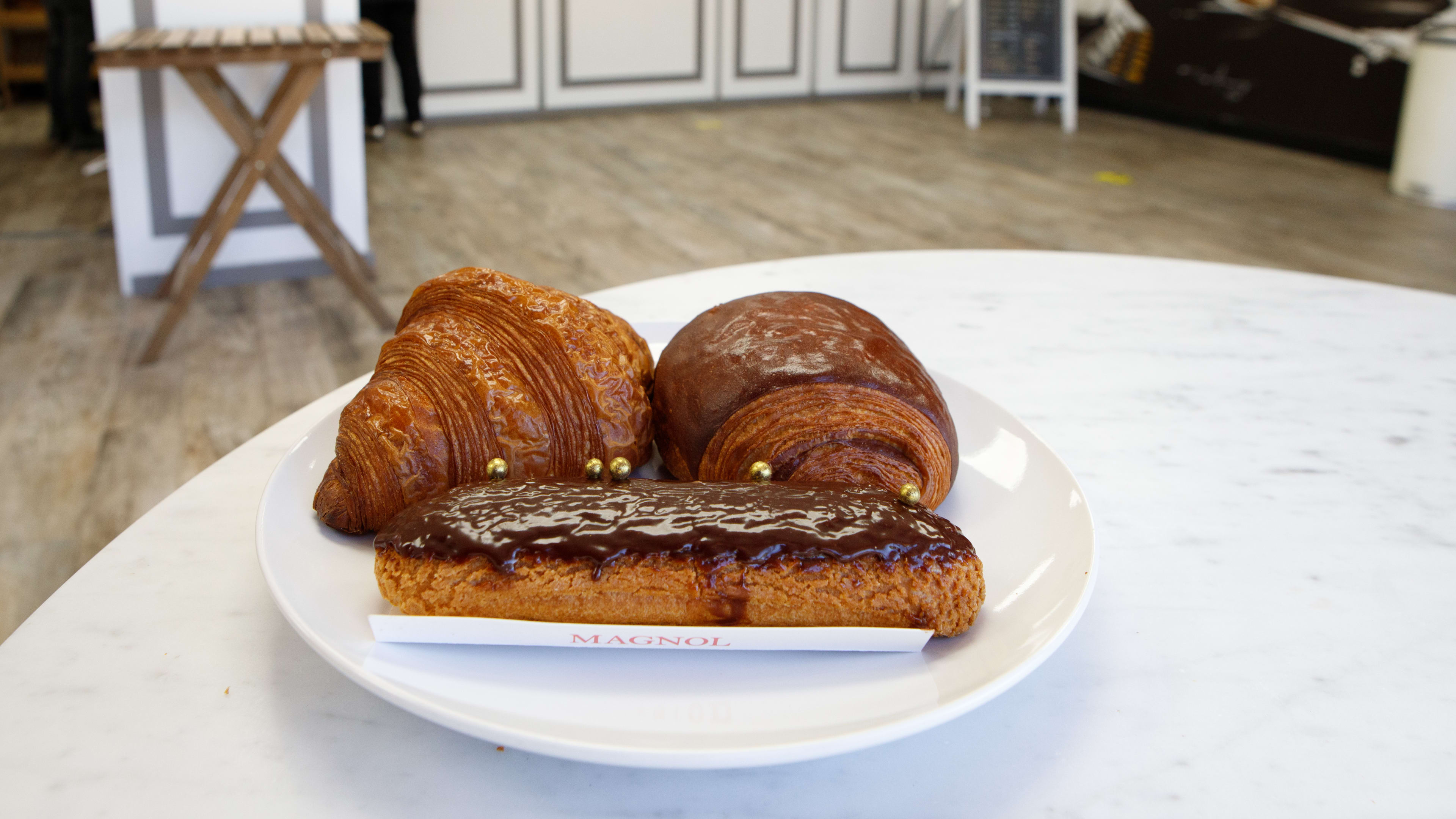 A spread of two croissants and an eclair on a plate at Magnol.