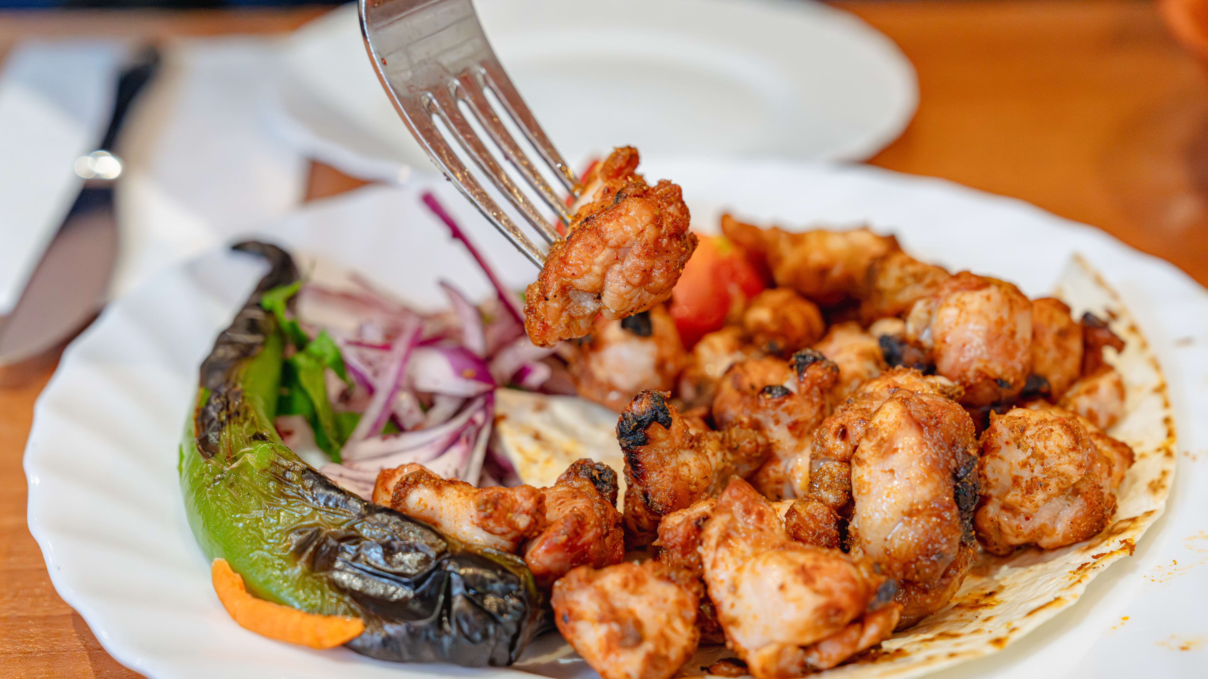 A fork digs into a white plate of sweetbreads and a large green pepper from Mangal 1.