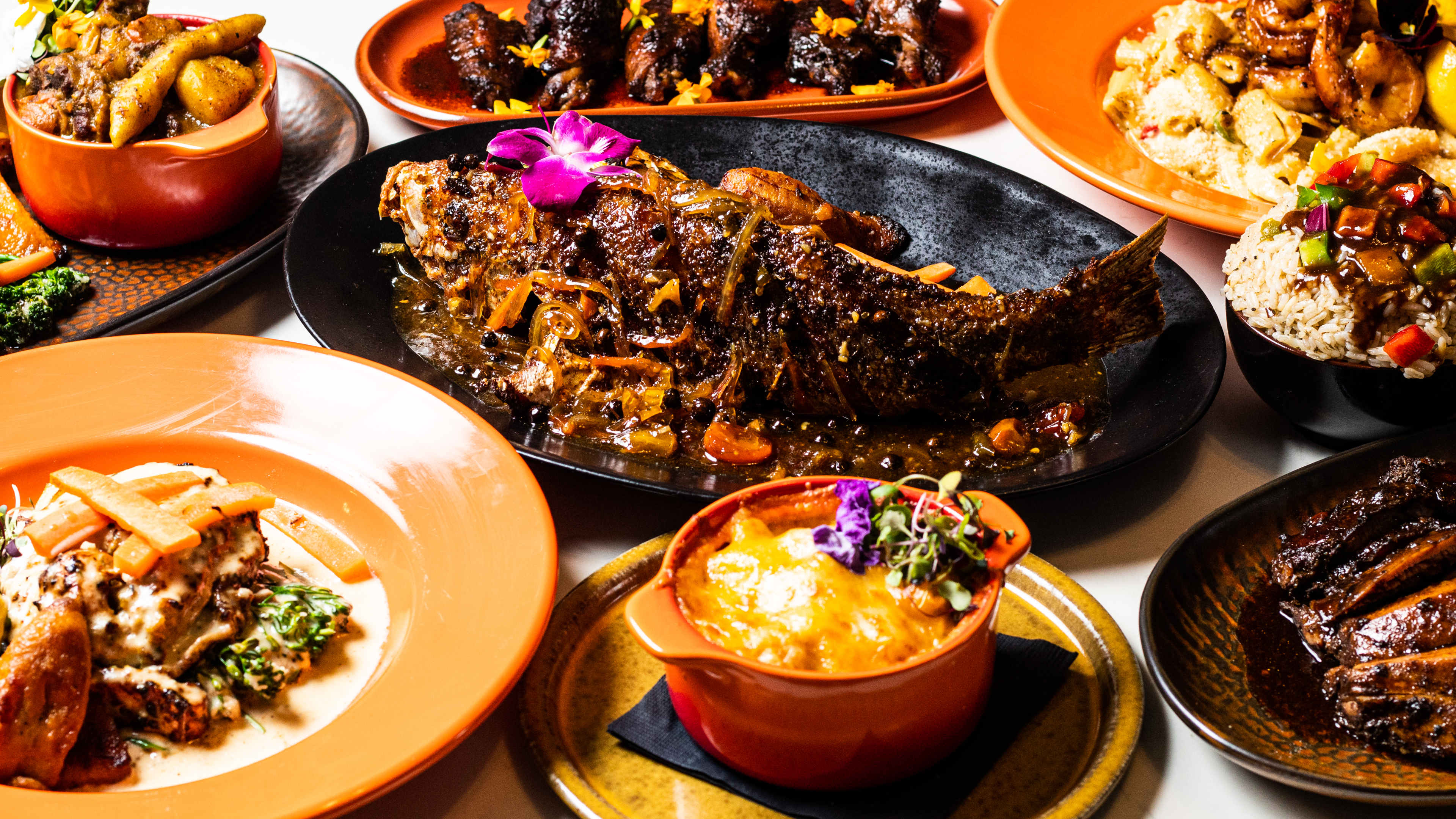 Series of Caribbean dishes garnished with flowers including a whole fried snapper in the middle.