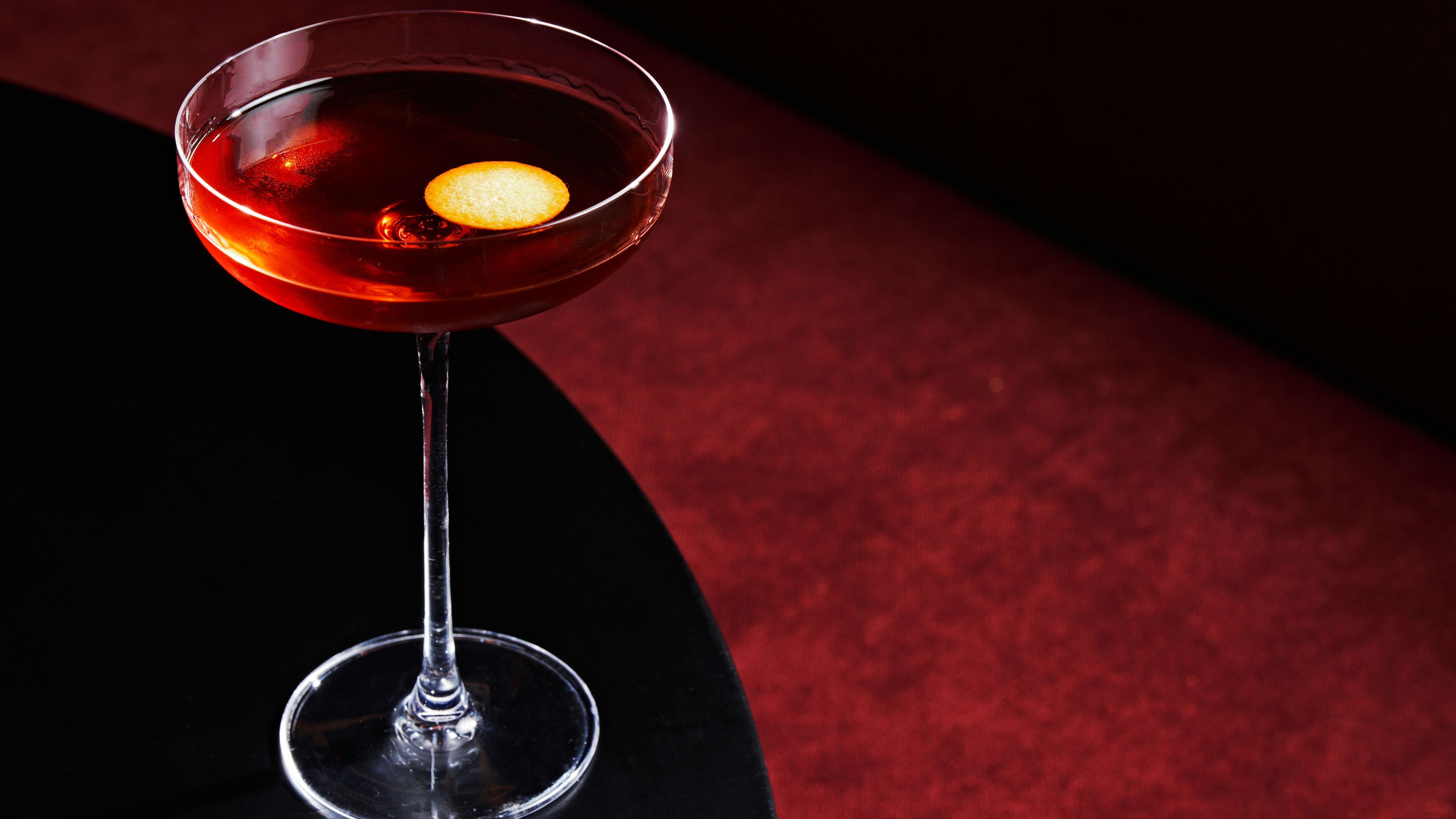 A whiskey cocktail served in a tall stemmed coupe with a round orange twist floating on top.