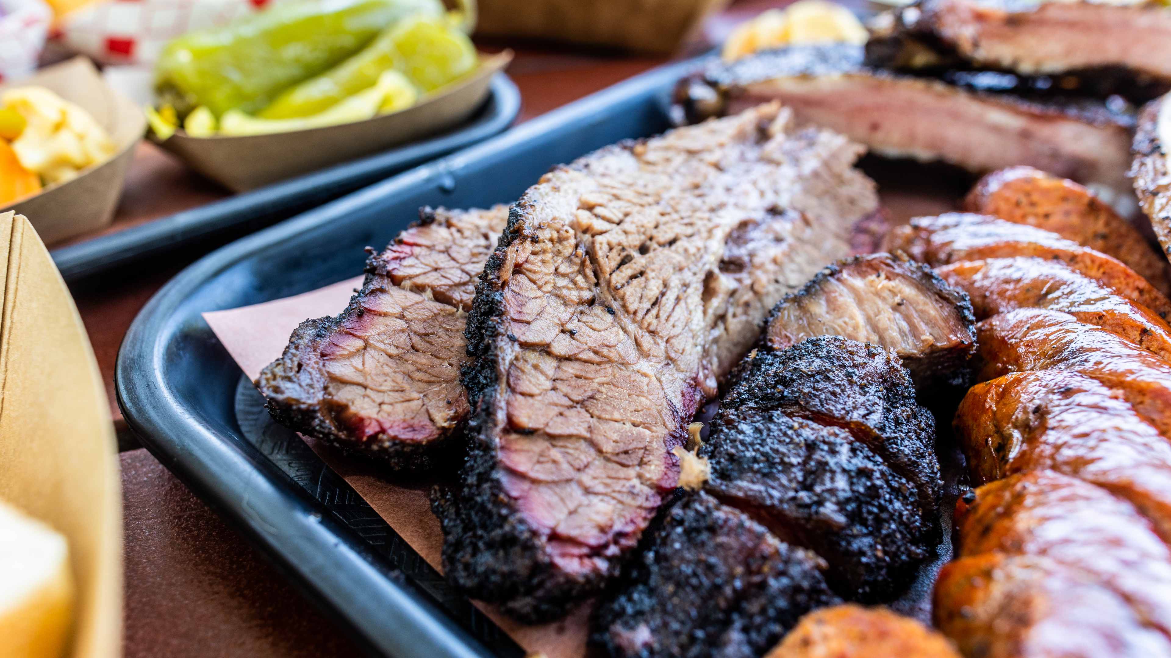 Brisket on a black lunch tray, surrounded by other meats and sides.